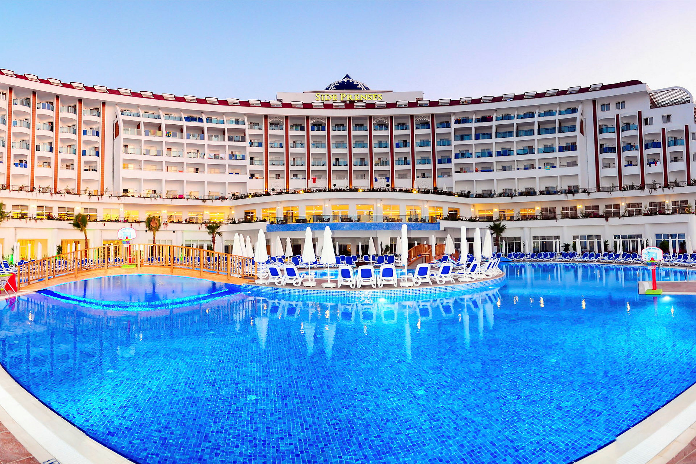 Hotellbyggnad med solstolar vid en stor utomhuspool. (AI-genererad text)