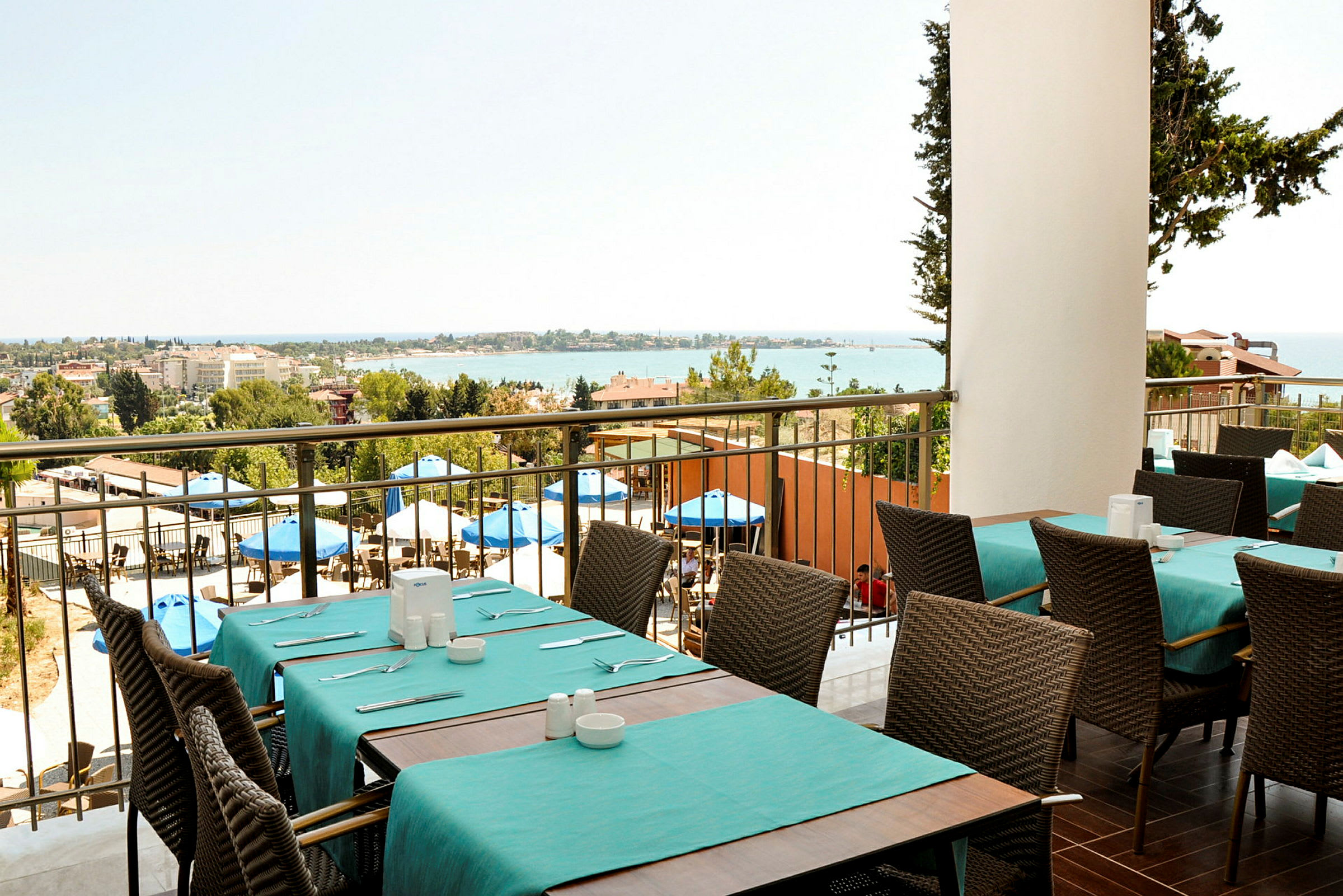 Utsikt från en restaurang med dukade bord och stolar, utomhusområde med parasoller och havet i bakgrunden. (AI-genererad text)