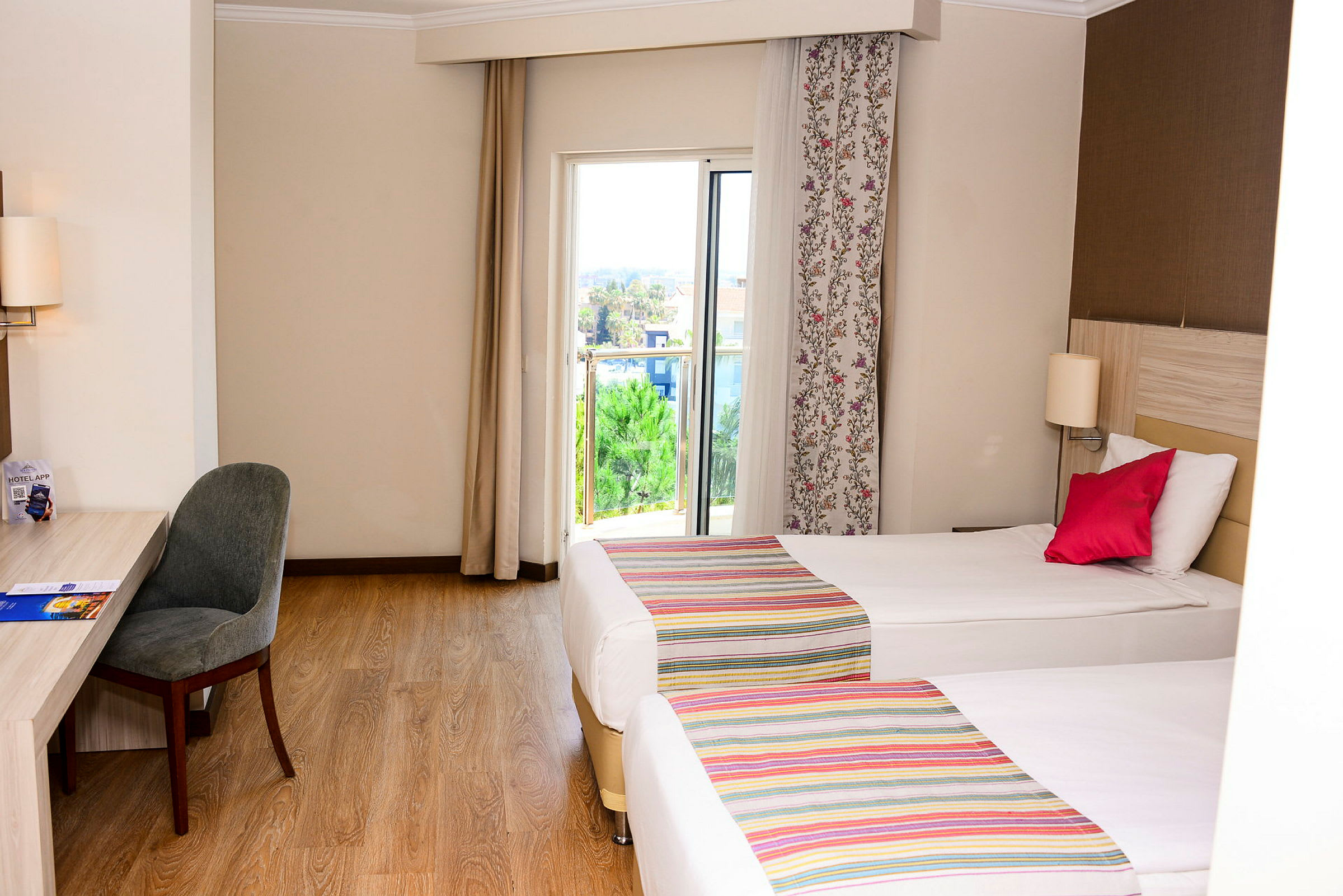 Ett hotellrum med två enkelsängar, ett skrivbord med en stol och en balkongdörr med utsikt. (AI-genererad text)