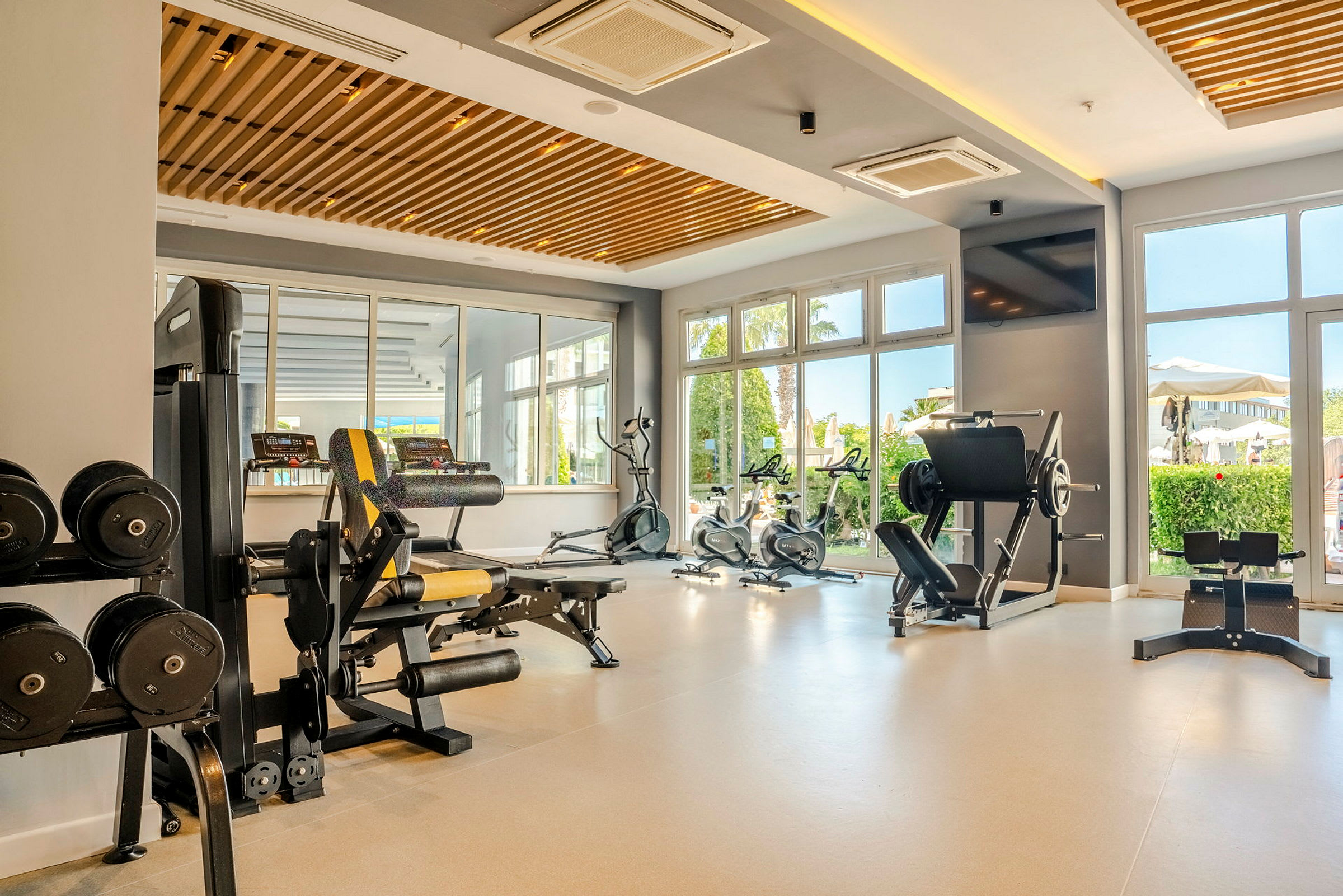 Ett gym med olika träningsmaskiner, hantlar och stora fönster som släpper in naturligt ljus. (AI-genererad text)