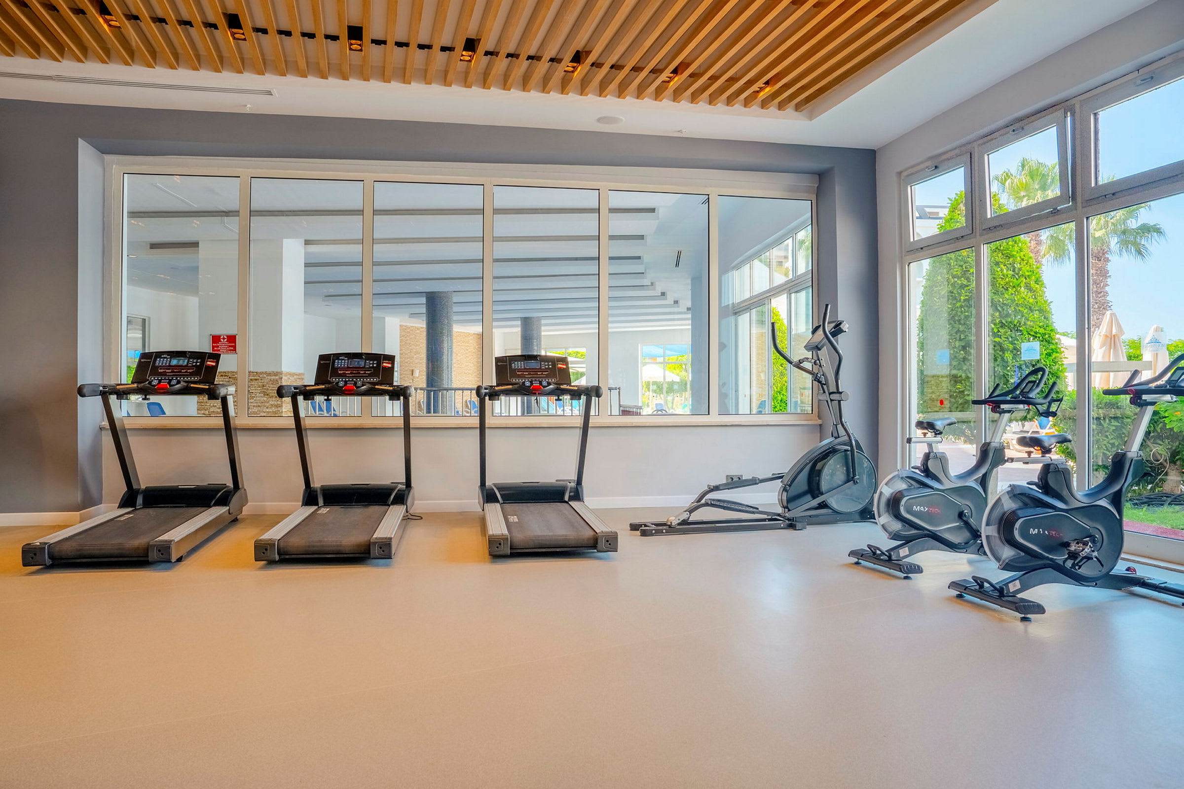 Ett gym med löpband, träningscyklar och stora fönster med utsikt utomhus. (AI-genererad text)