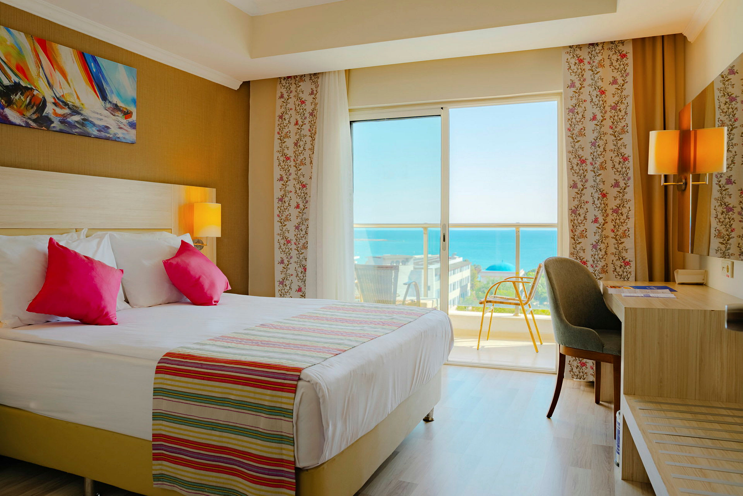 Hotellrum med dubbelsäng, skrivbord och balkongutsikt över havet. (AI-genererad text)