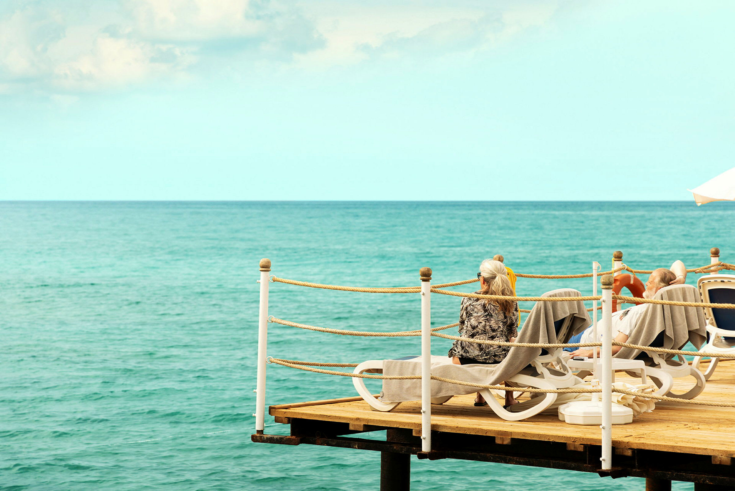 Personer som sitter på solstolar på en brygga vid havet. (AI-genererad text)