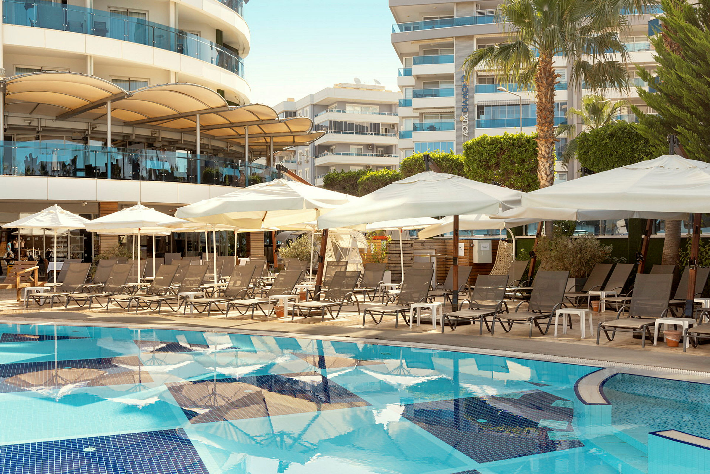 Poolområde med solstolar och parasoller framför hotellbyggnader. (AI-genererad text)