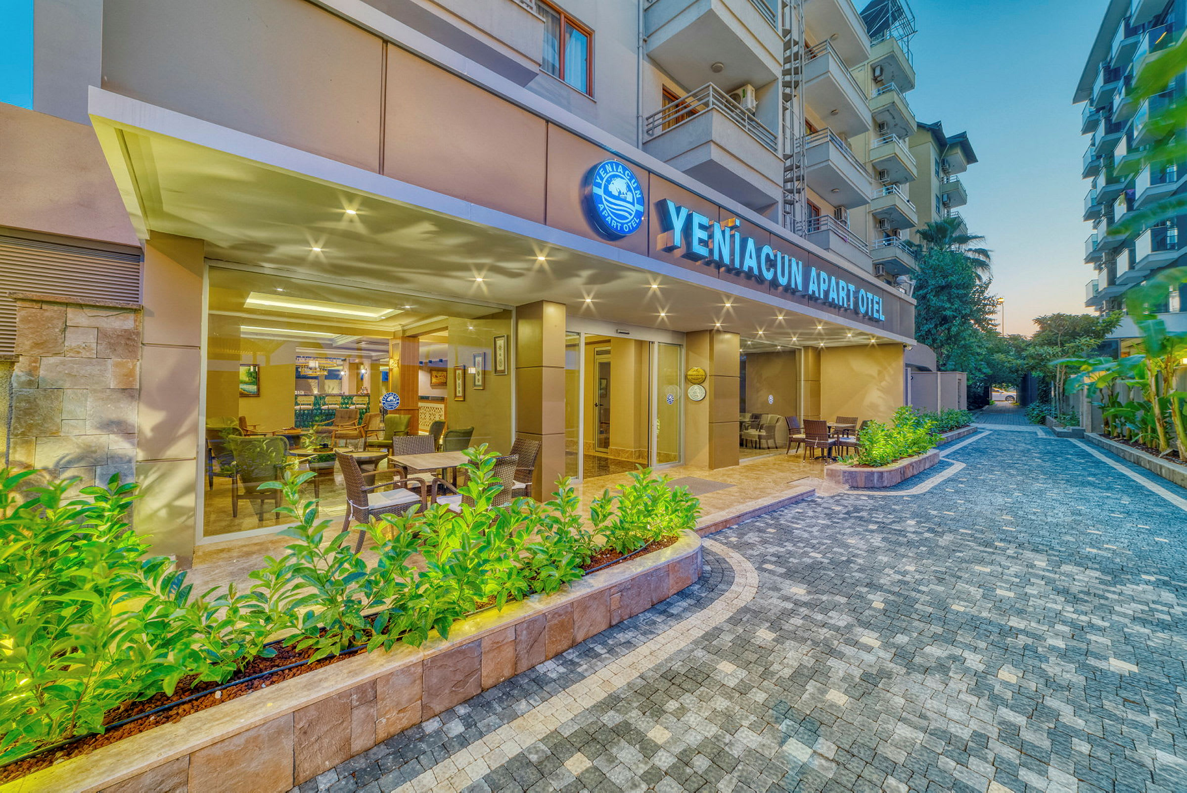 Exteriör av YenĂ?acun Apart Otel med utomhusbänkar och grönska. (AI-genererad text)