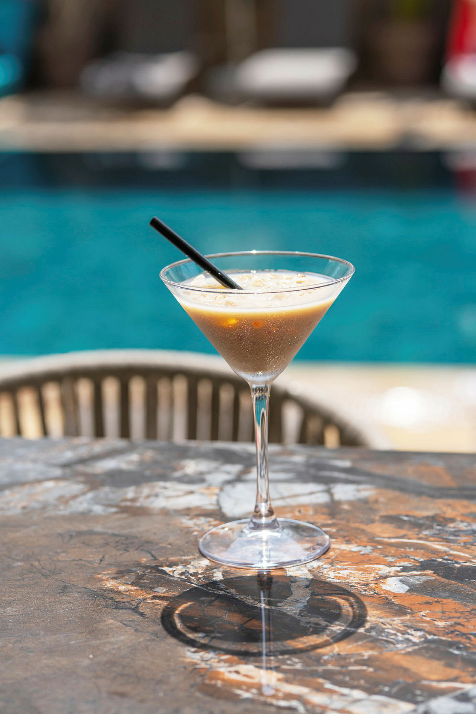 Ett glas med en kall drink står på ett bord nära en pool. (AI-genererad text)