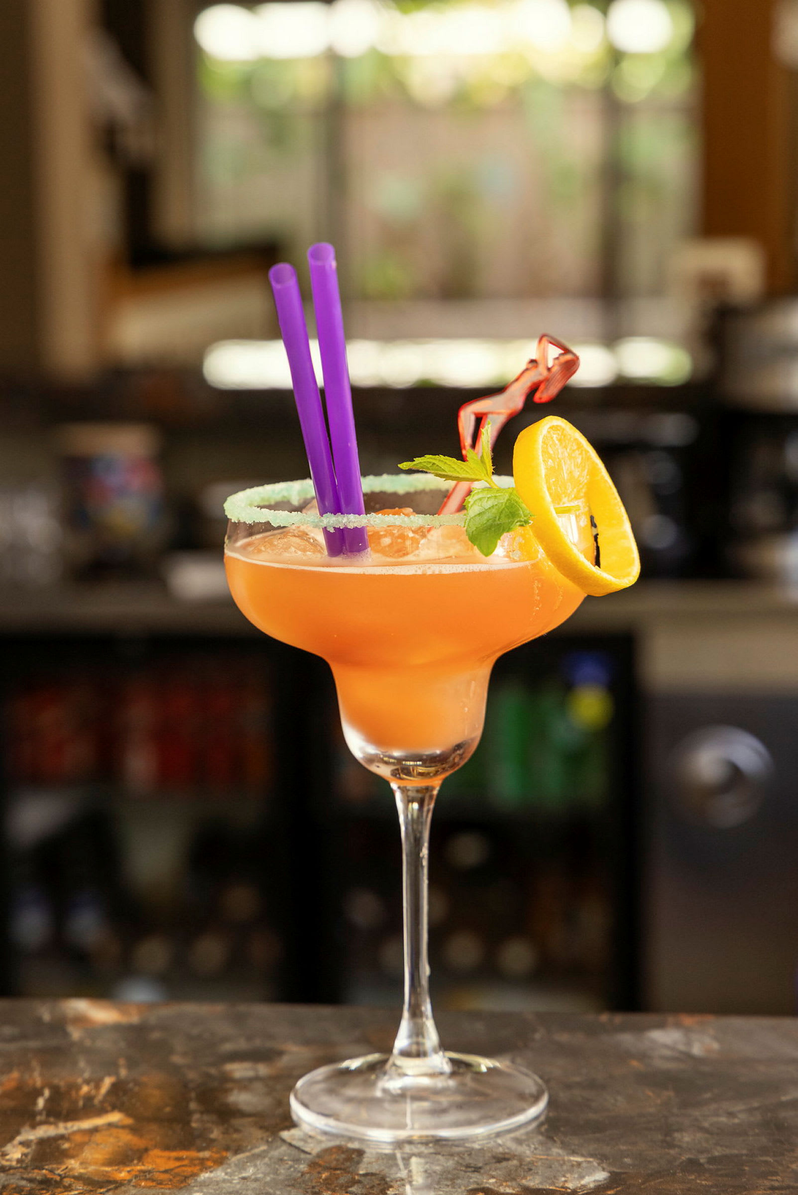 En cocktail serverad i ett glas med en citronskiva, myntablad och sugrör. (AI-genererad text)