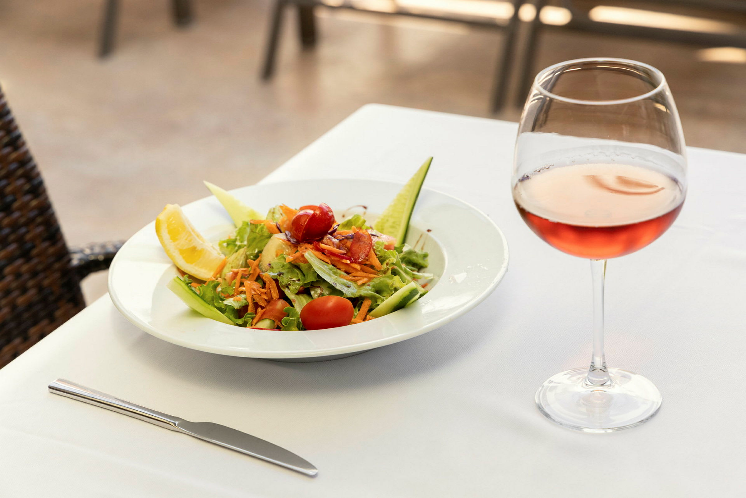 En tallrik med sallad och ett glas rosévin på ett dukat bord. (AI-genererad text)