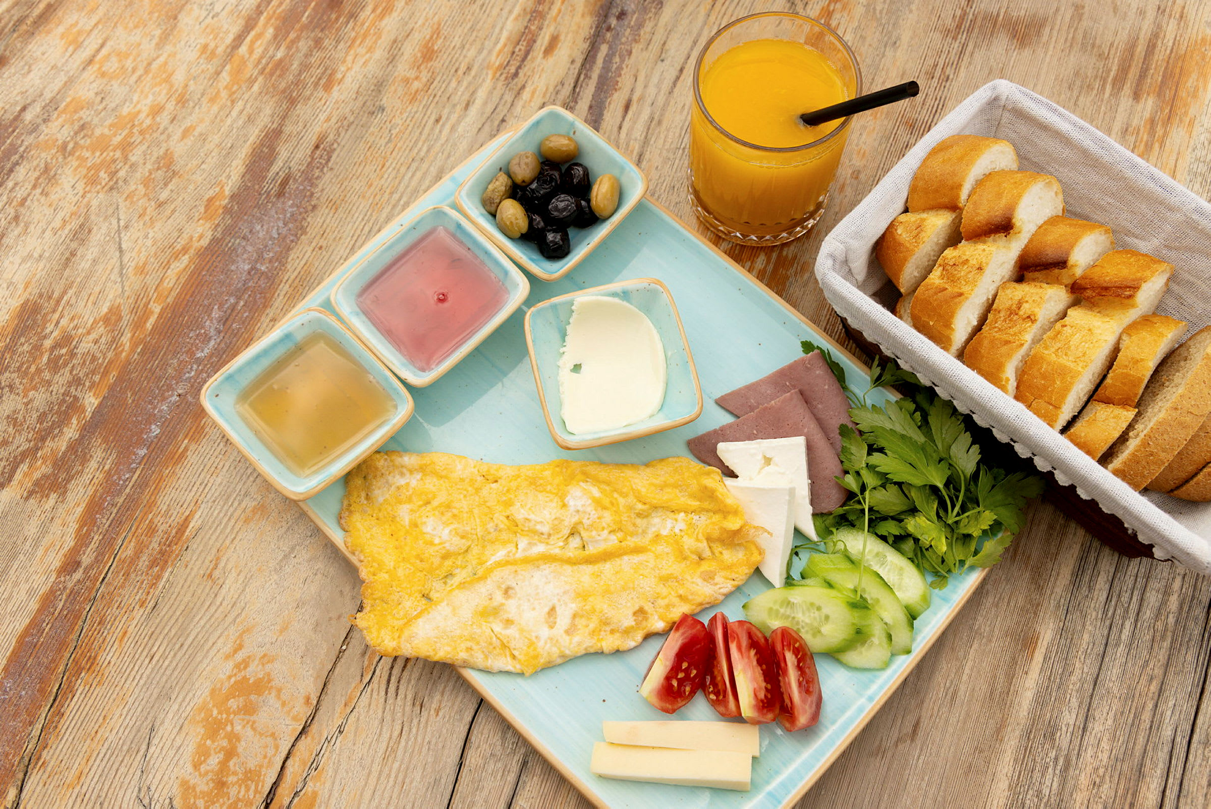 En frukost med omelett, grönsaker, ost, bröd, oliver och apelsinjuice. (AI-genererad text)