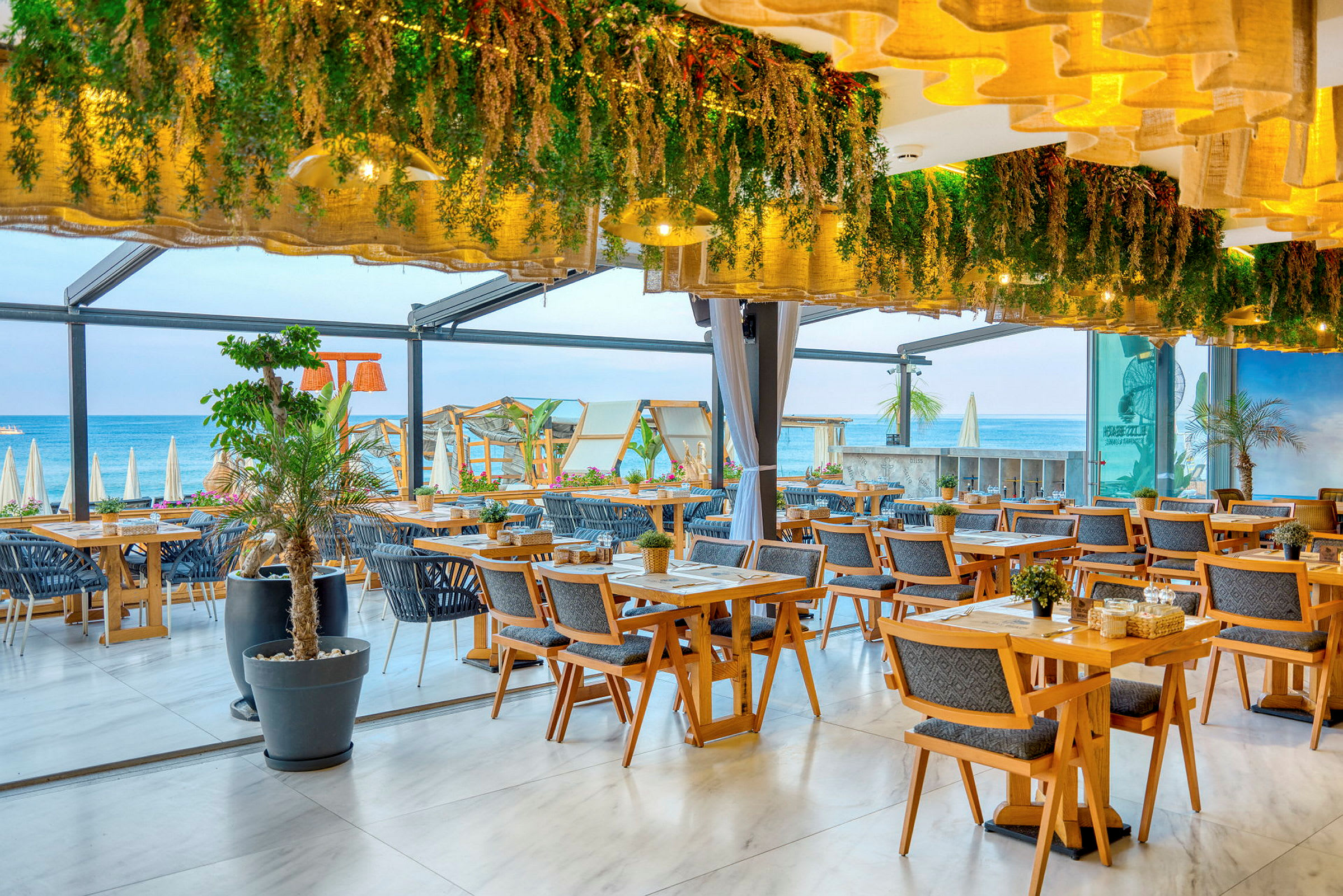 Restaurang med träbord, dekorativa växter och utsikt mot stranden. (AI-genererad text)