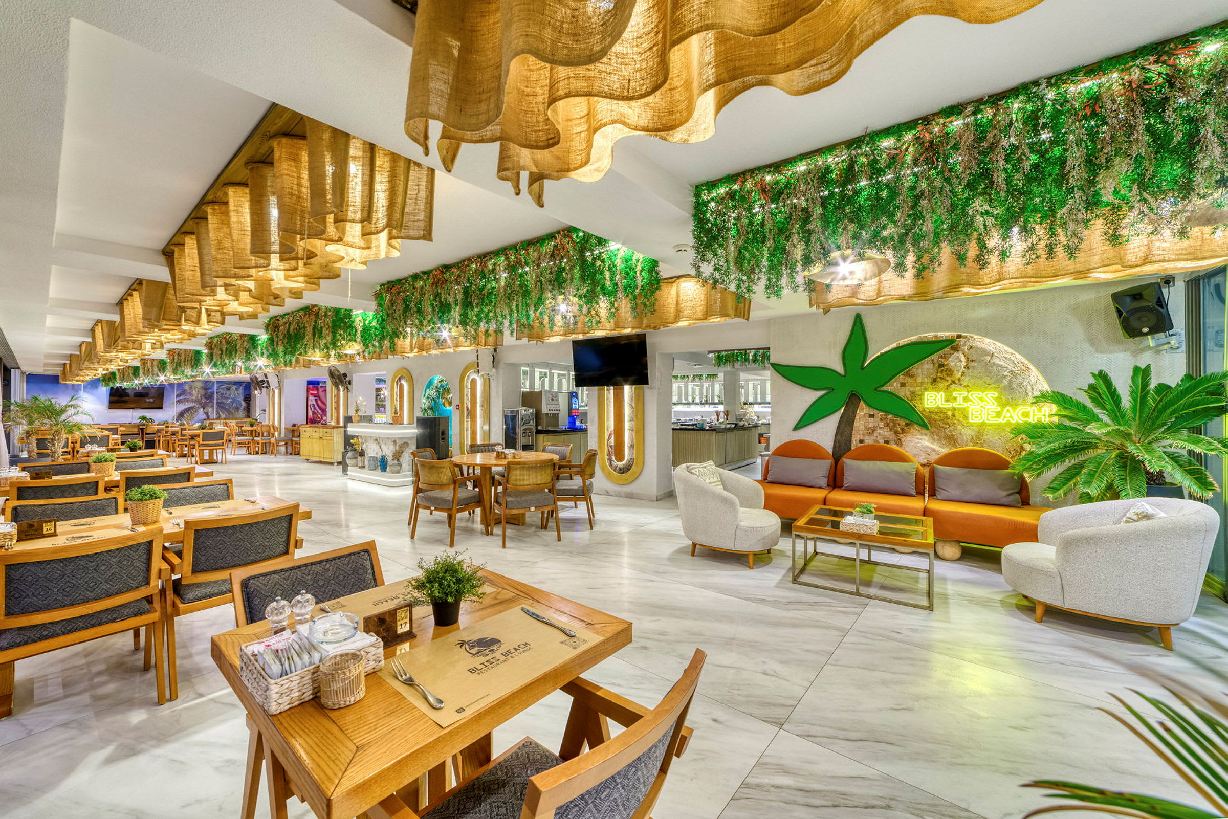 Interiör av en restaurang med sittgrupper, gröna dekorationer och en skylt som lyser med texten Bliss Beach. (AI-genererad text)