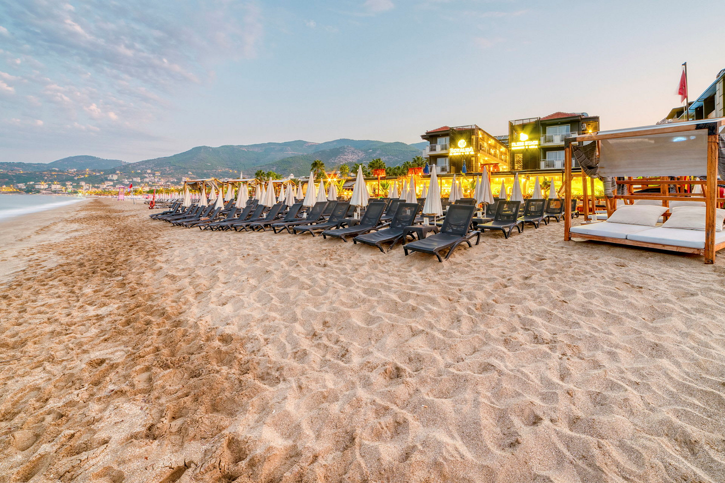 Solstolar och parasoller på en sandstrand med hotell i bakgrunden. (AI-genererad text)