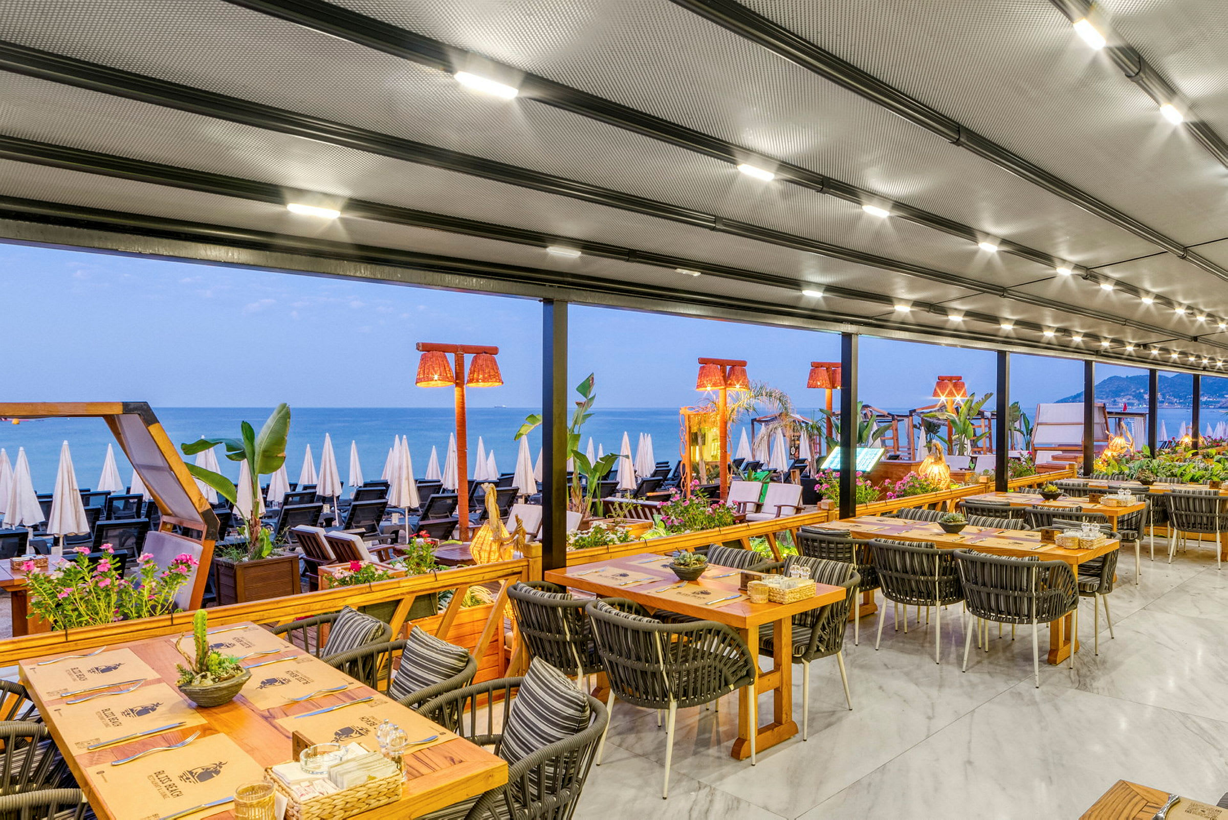 En restaurang med utsikt över en strand och havet, borden är dukade för måltid. (AI-genererad text)