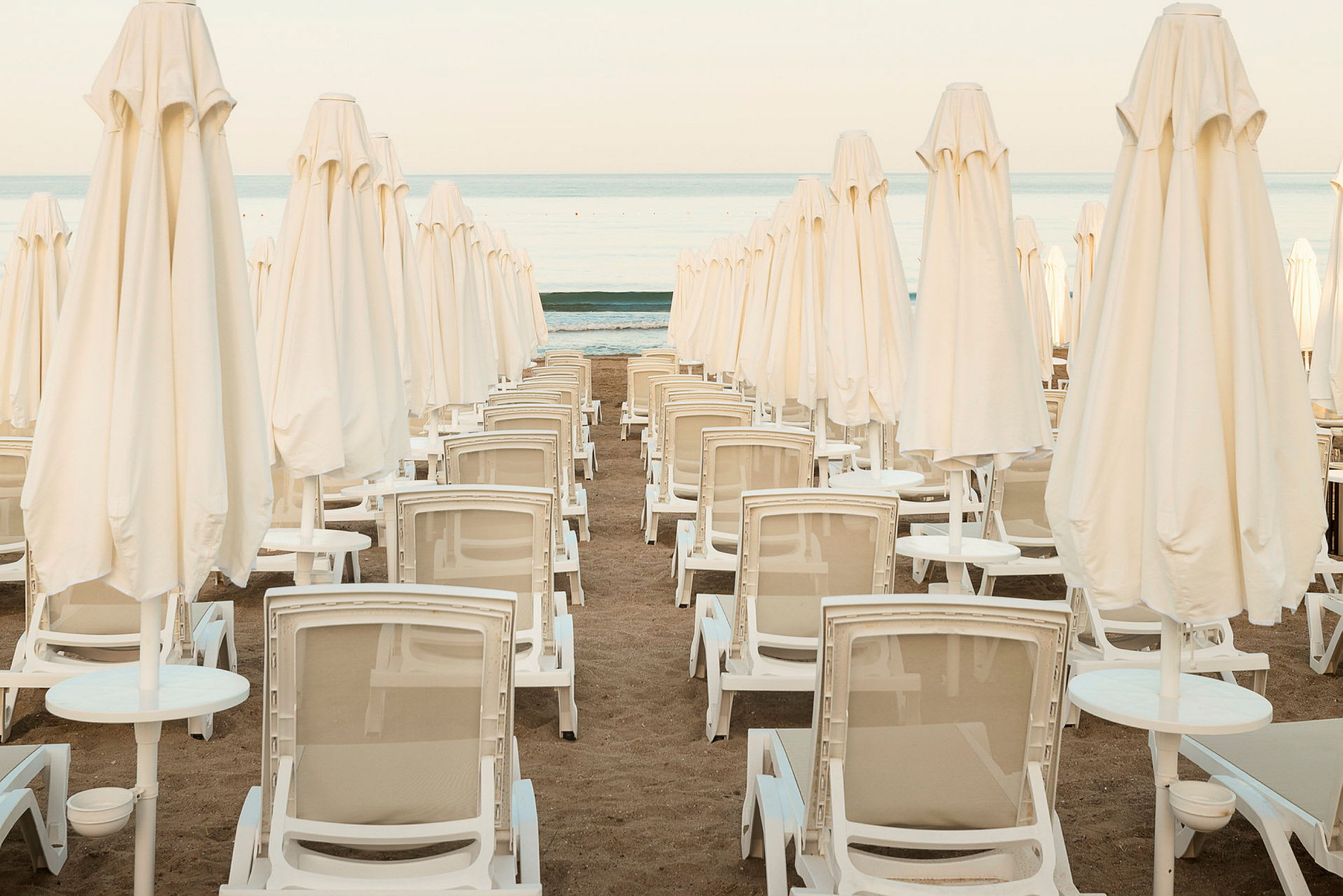 Flera solstolar och strandparasoller i rad på sandstrand. (AI-genererad text)