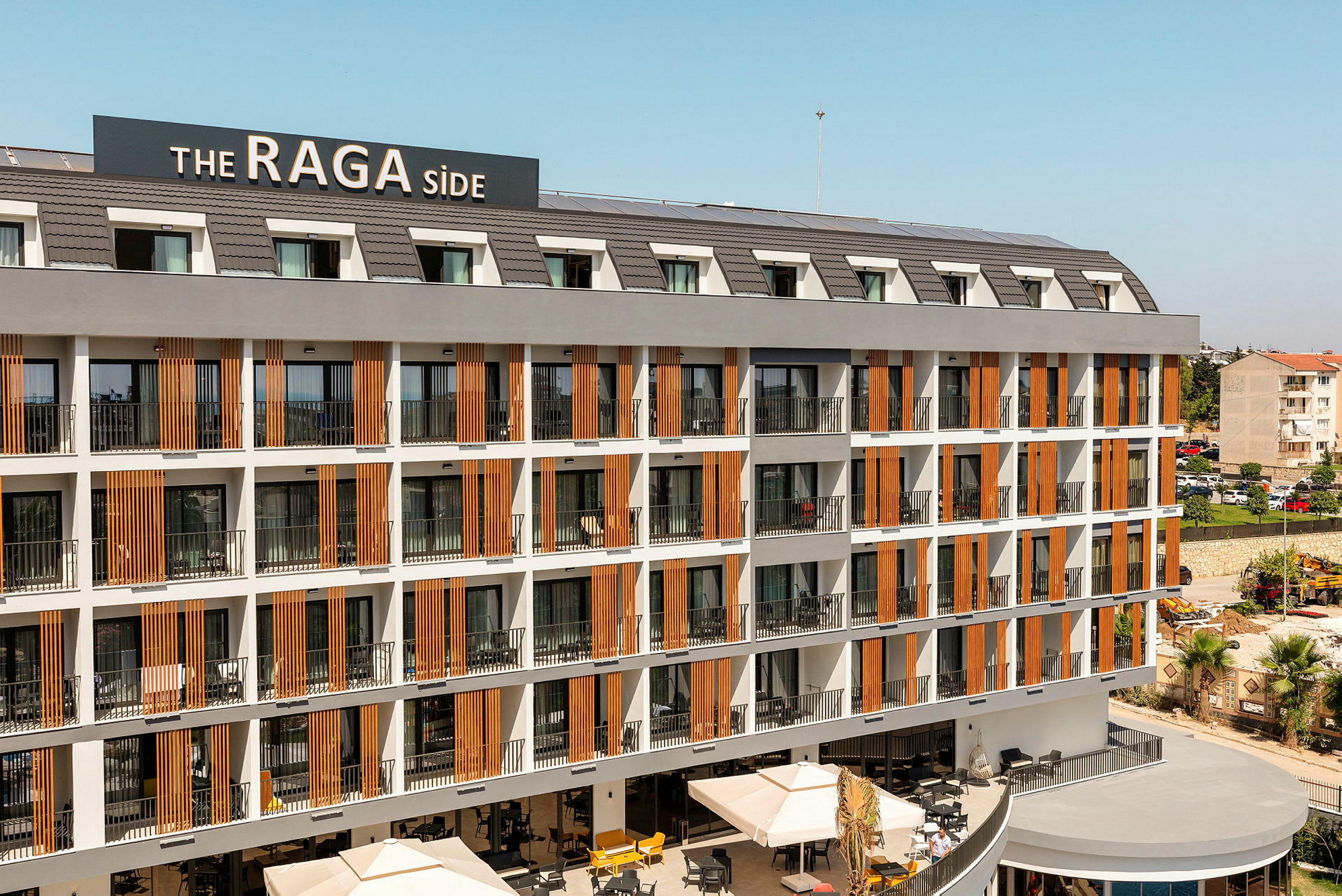 Hotellkomplex med flera våningsplan med balkonger och en skylt som visar namnet 'The RAGA Side'. (AI-genererad text)