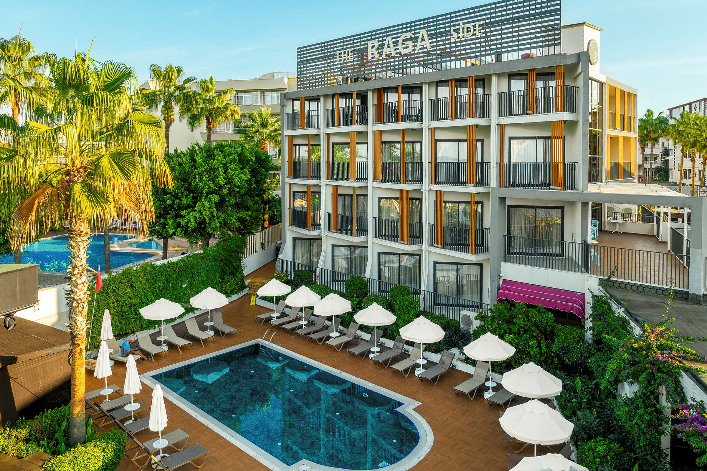 En hotellbyggnad med flera balkonger och en pool vid dess bas, omgiven av solstolar och parasoller. (AI-genererad text)