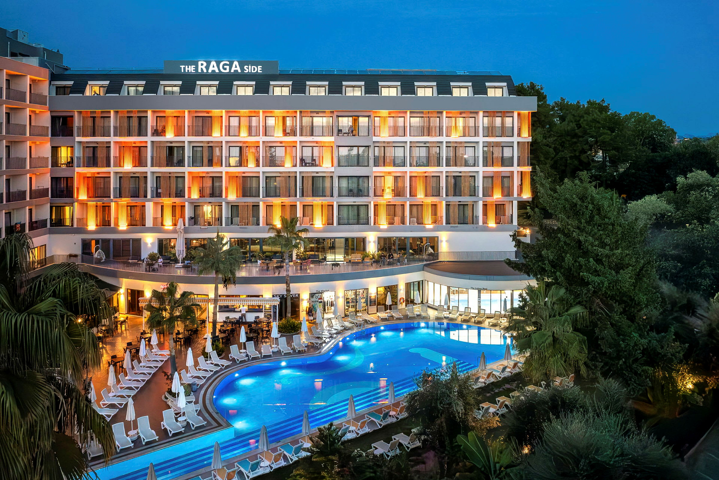 Hotellfasad vid skymning med upplysta balkonger och en pool omgiven av solstolar. (AI-genererad text)