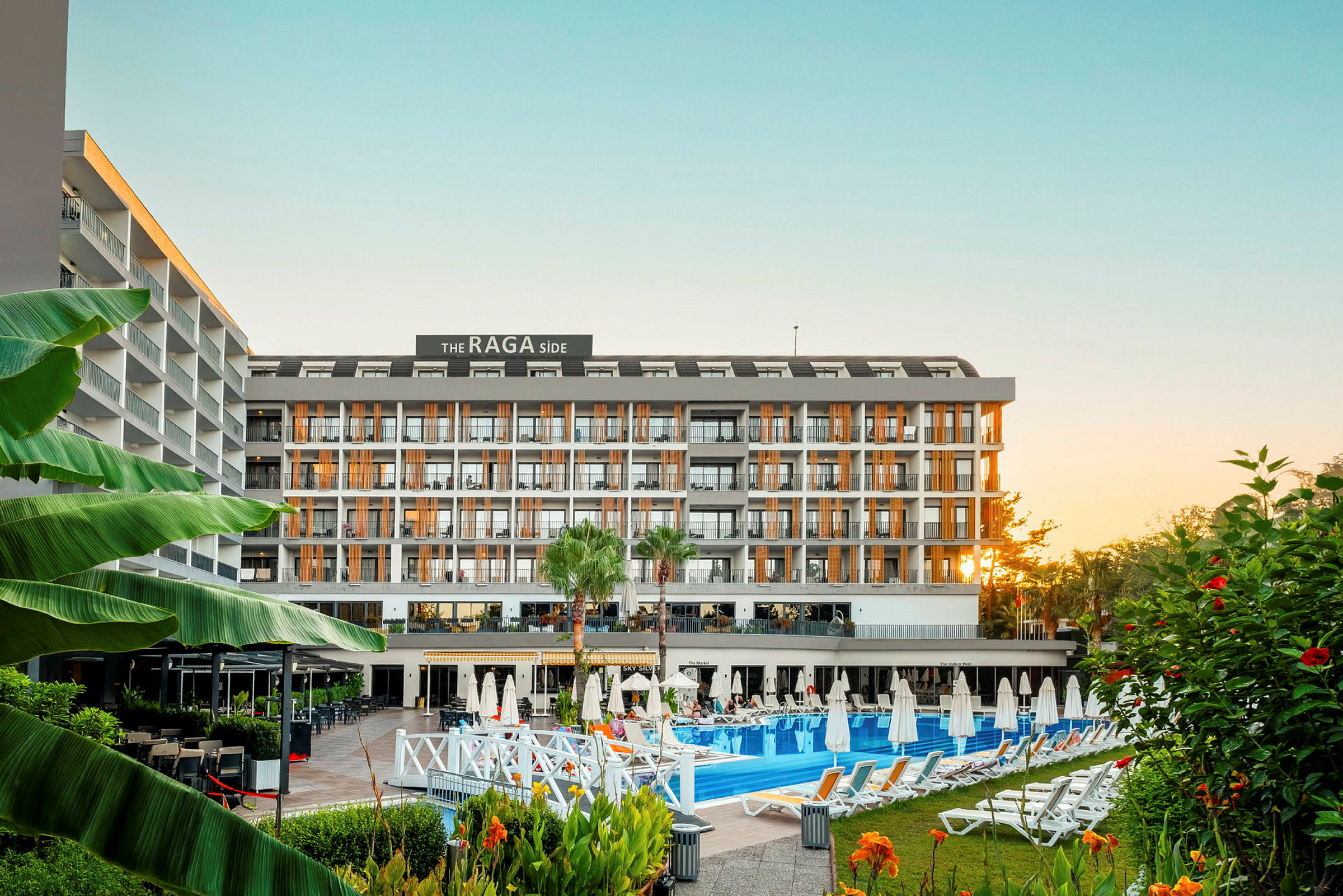 Ett hotellkomplex med flera våningar sett framifrån, omgivande pool, solstolar och grönska. (AI-genererad text)
