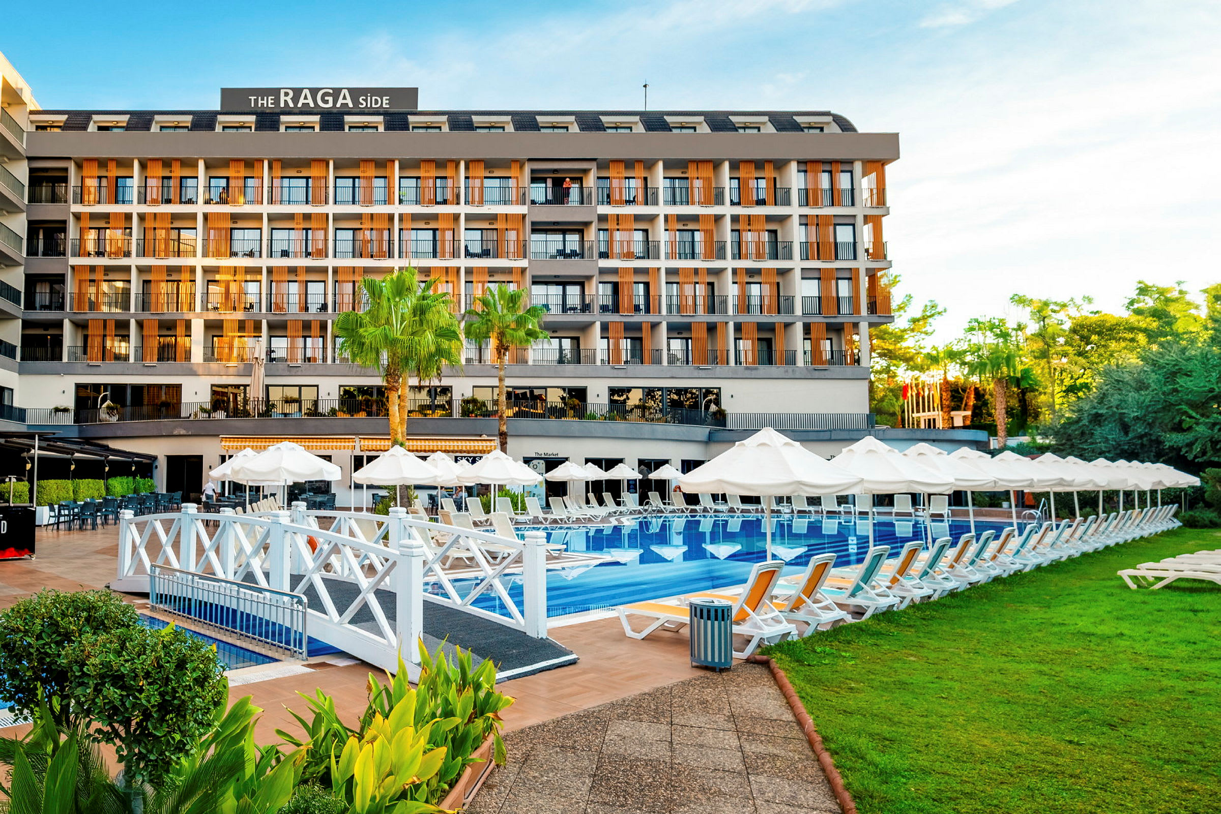 Ett hotell med en pool framför, omgivet av solstolar och grönska. (AI-genererad text)