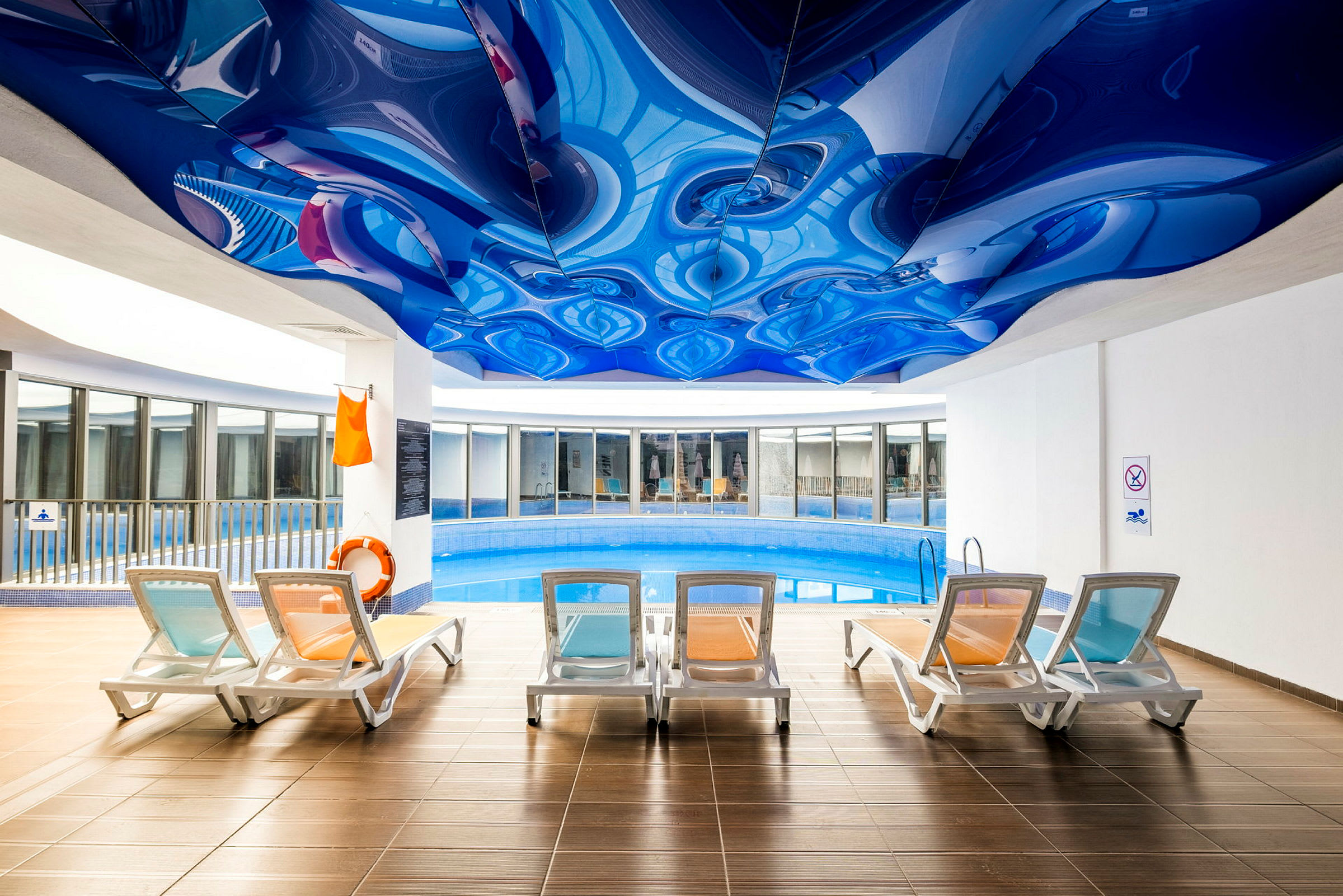 Inomhuspool med flera solstolar och ett blått unikt mönstrat tak. (AI-genererad text)