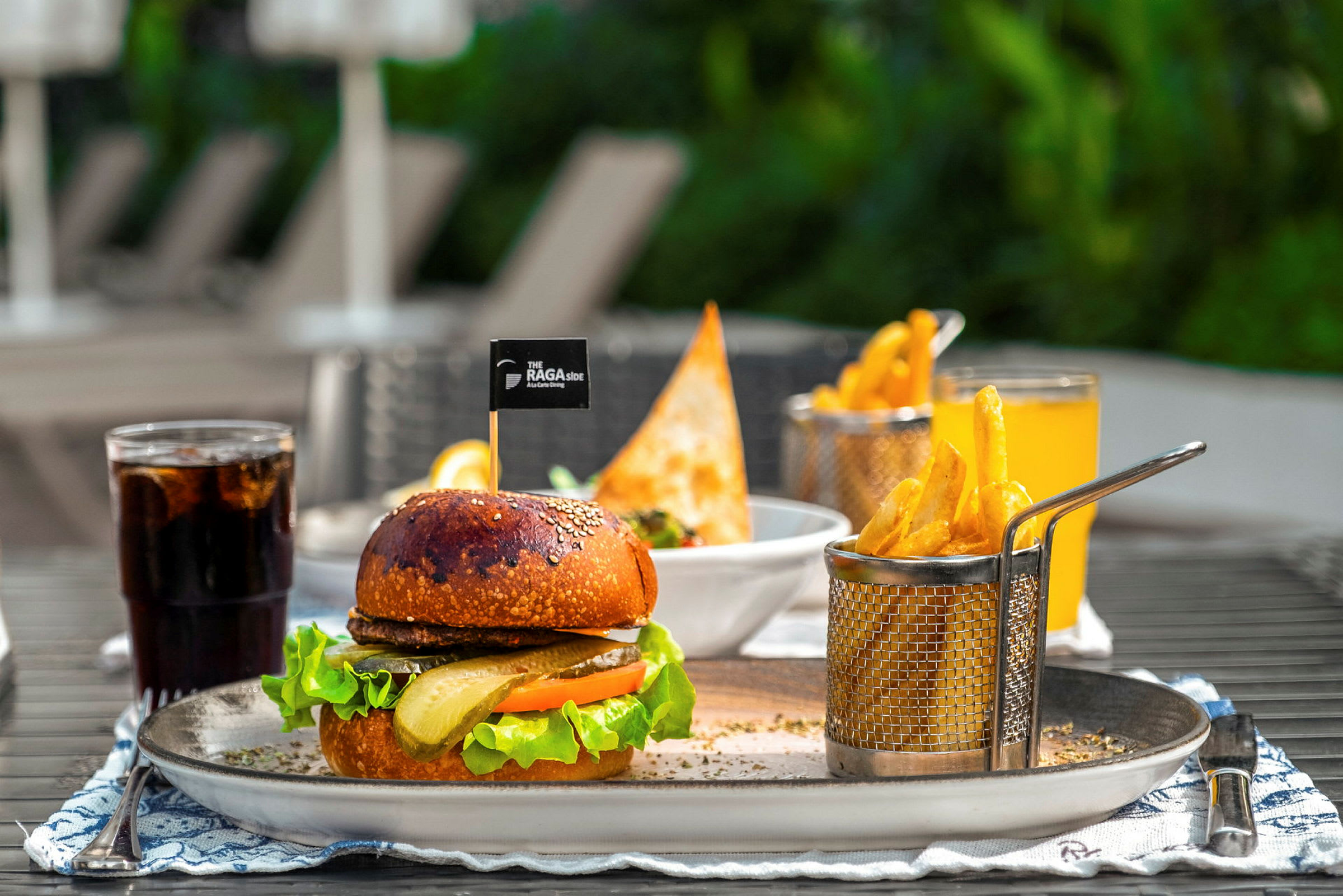 En tallrik med en hamburgare, pommes frites och dryck utomhus. (AI-genererad text)