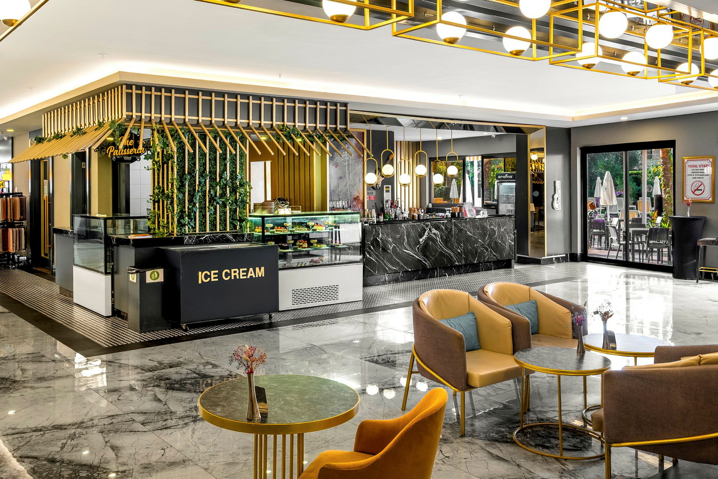 Ett modernt caféområde med glassdisk framträdande, guld- och svarta detaljer. Sittplatser med färgglada stolar och dekorativa bord. Ett rymligt och elegant golv av marmor. (AI-genererad text)