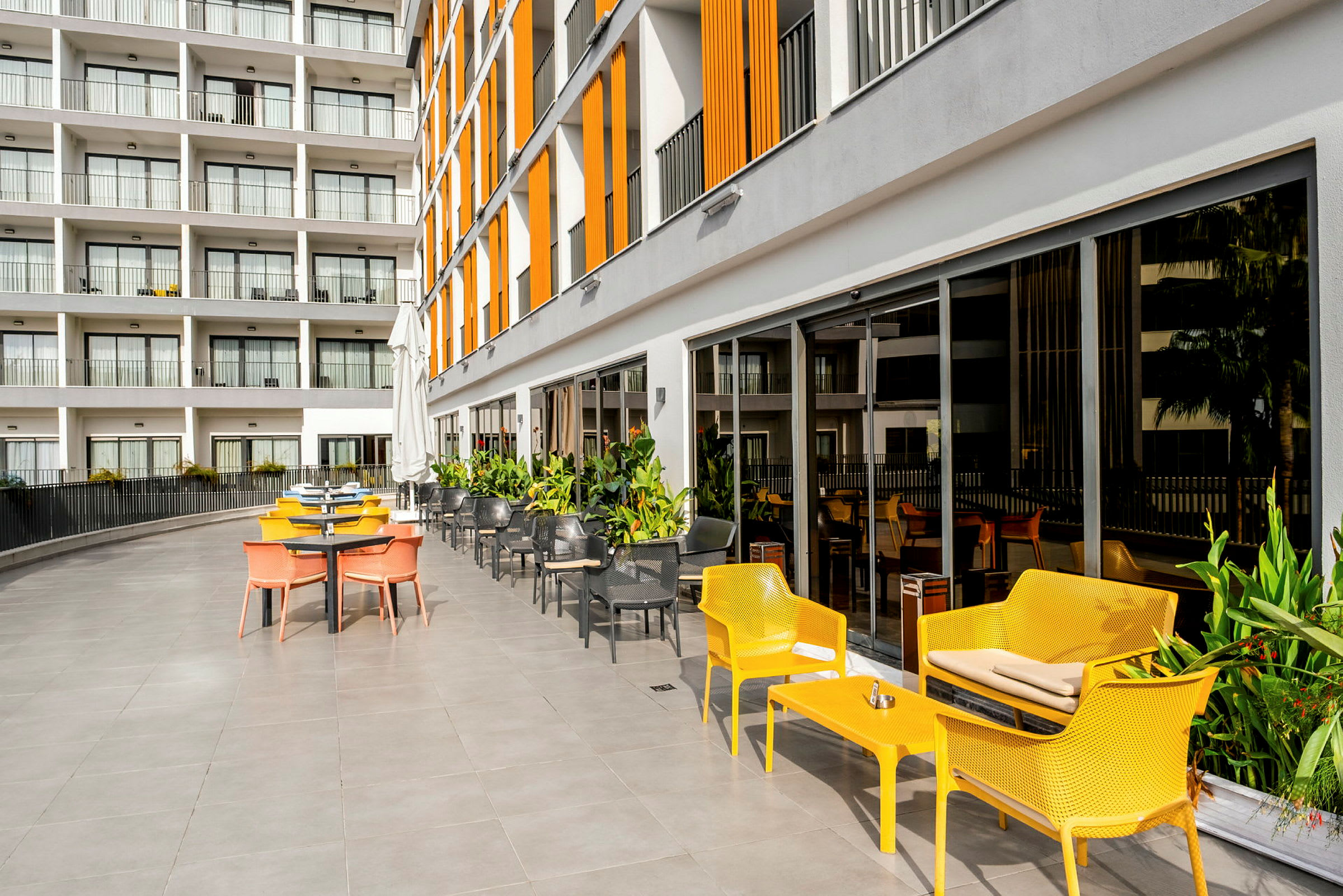 Uteservering med färgglada stolar och ett modernt hotell i bakgrunden. (AI-genererad text)