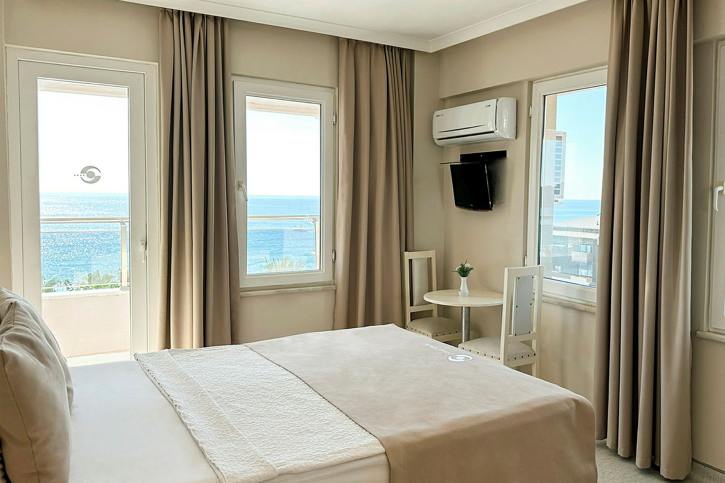 Ett hotellrum med en säng, ett runt bord med två stolar och fönster som vetter mot havet. (AI-genererad text)