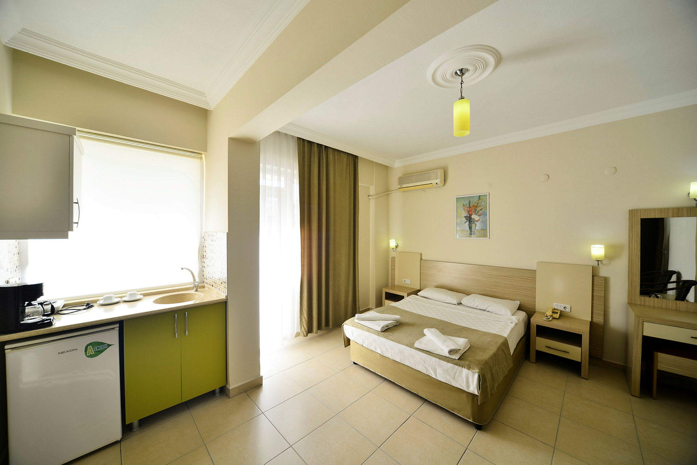 Ett hotellrum med en säng, sängbord, köksutrustning och ljusa väggar. (AI-genererad text)