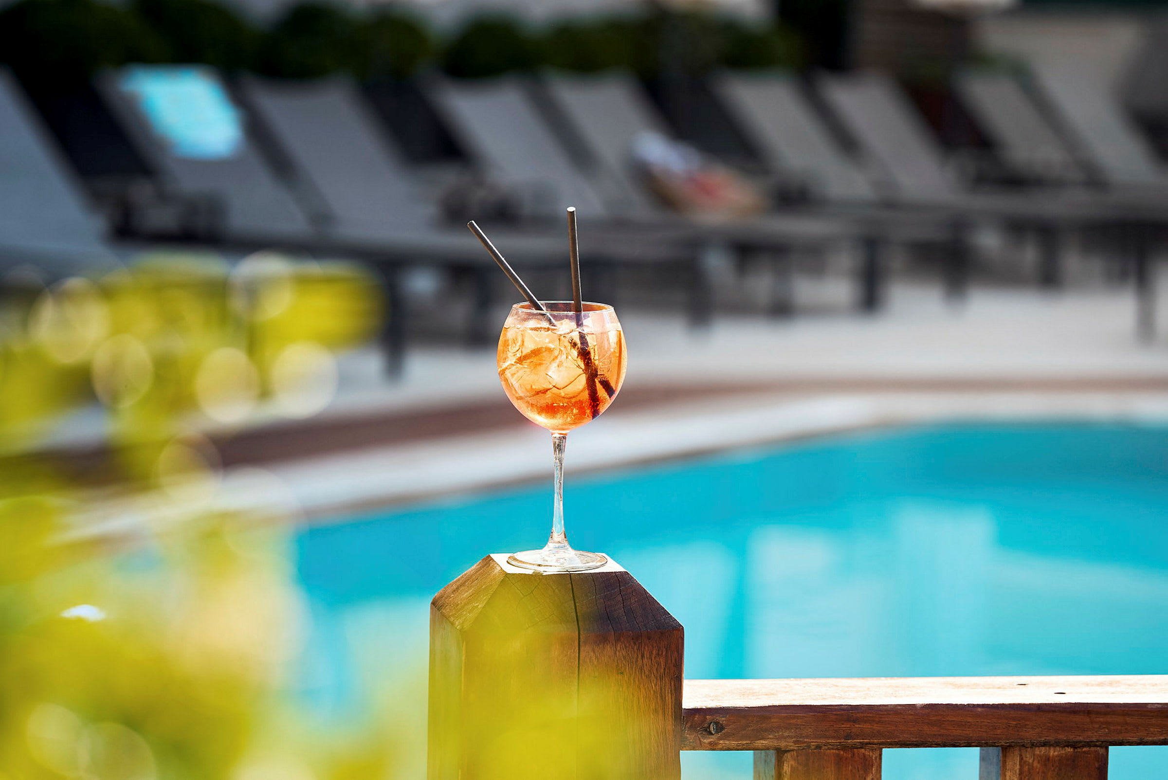 Ett glas drink står på ett trästaket vid en pool. (AI-genererad text)
