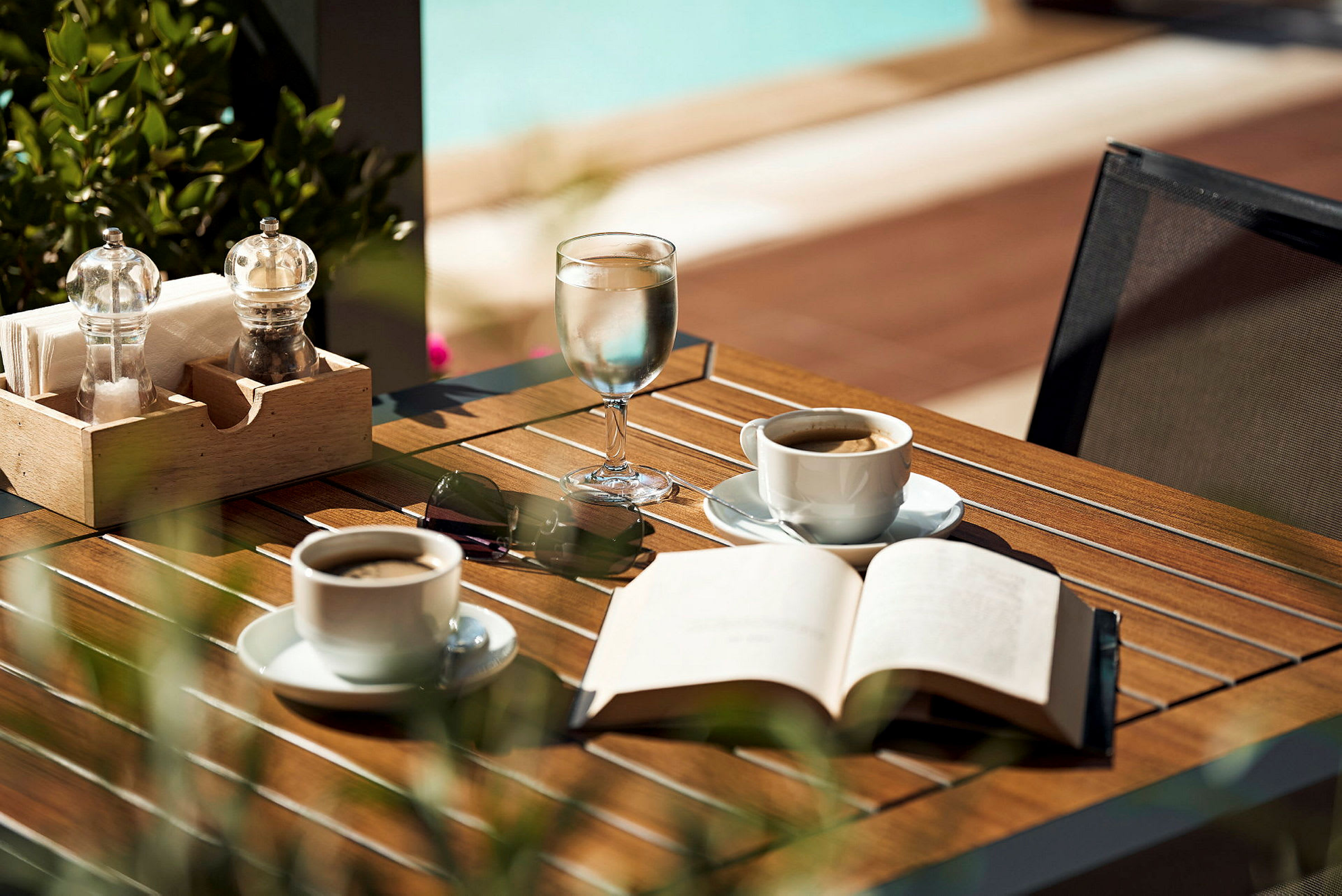Ett bord med kaffekoppar, ett glas vatten, en öppen bok och solglasögon. (AI-genererad text)