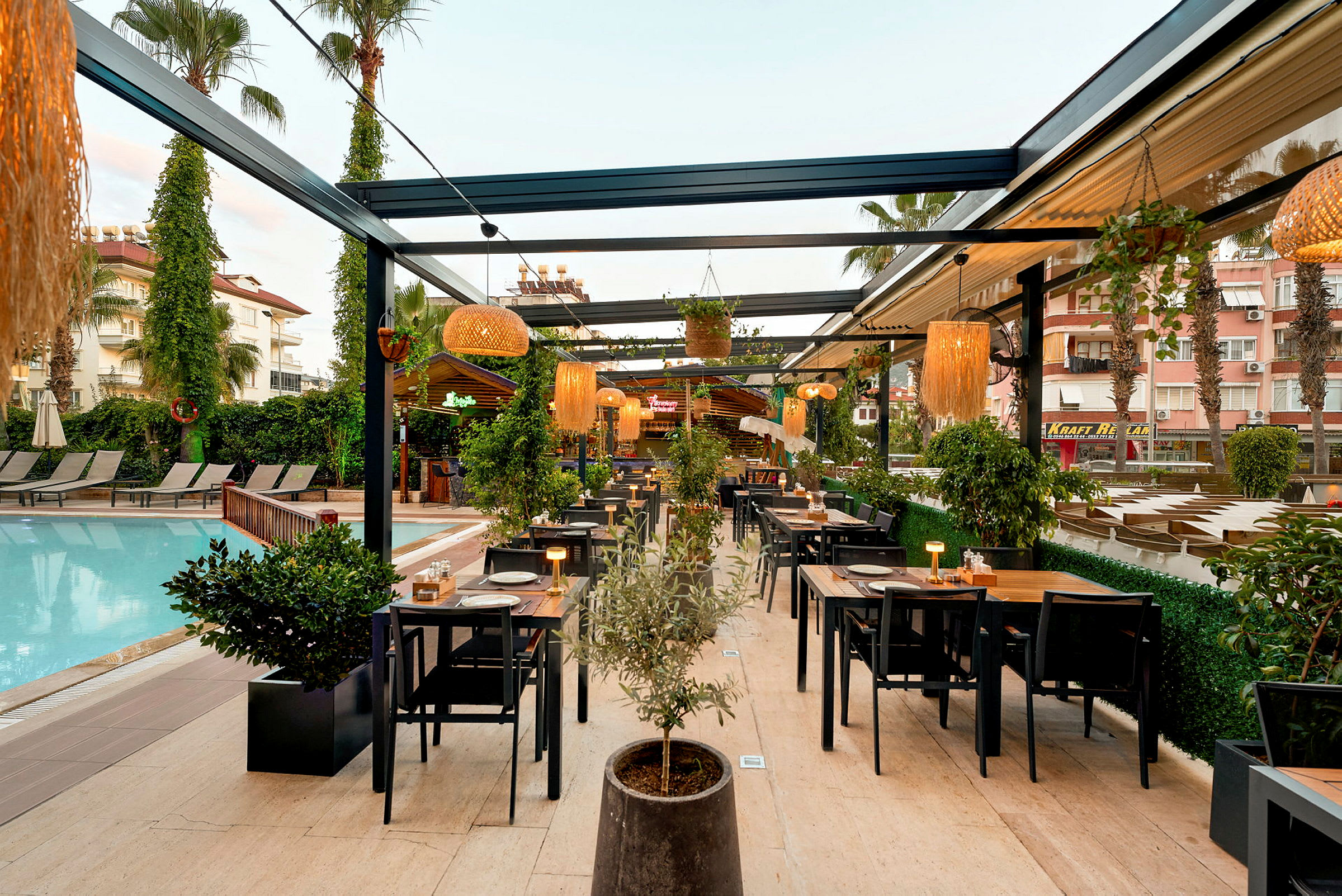 Utomhusrestaurang intill en pool med bord och stolar samt växter och belysning. (AI-genererad text)