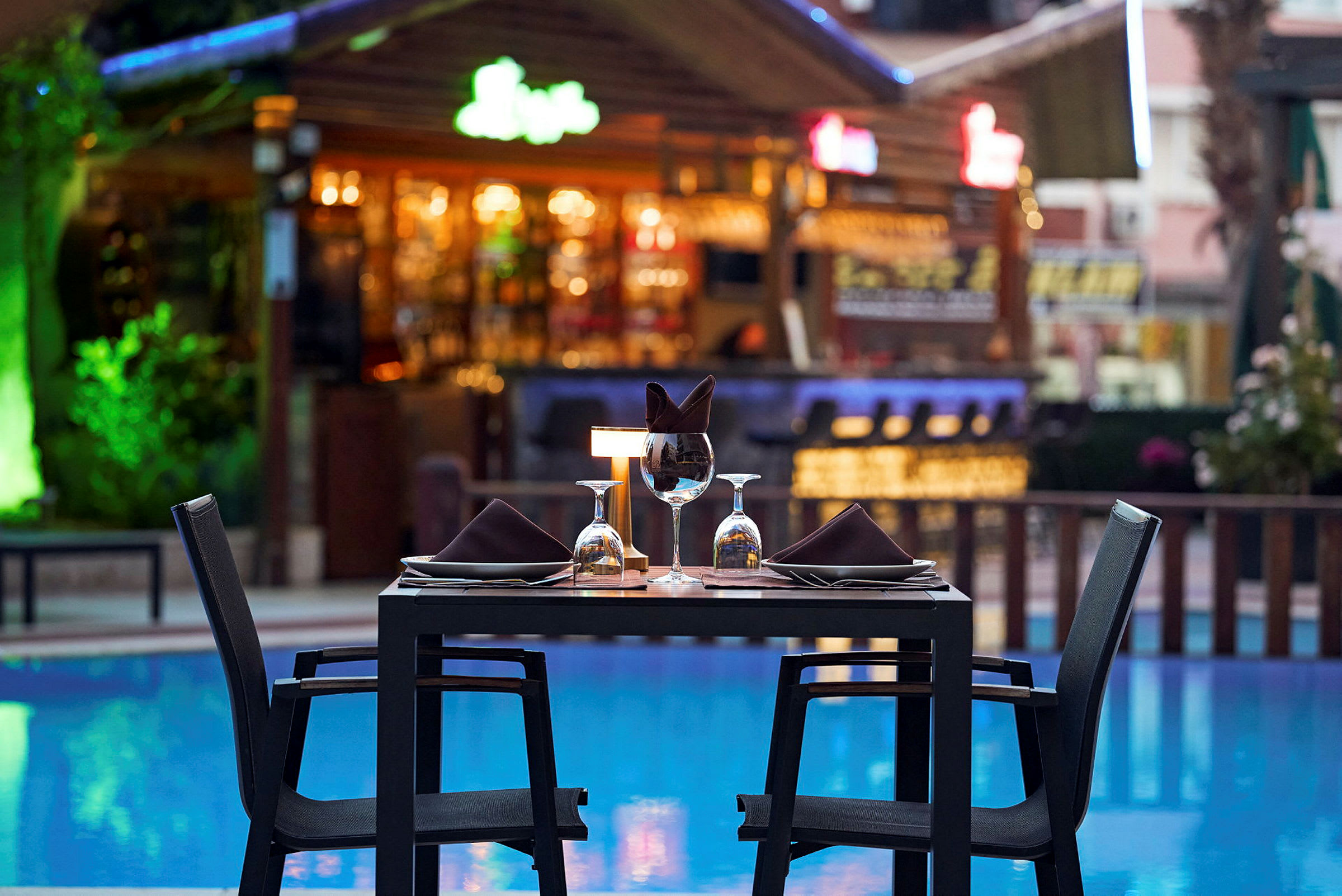 Ett bord med dukning vid en pool, i bakgrunden syns en bar. (AI-genererad text)