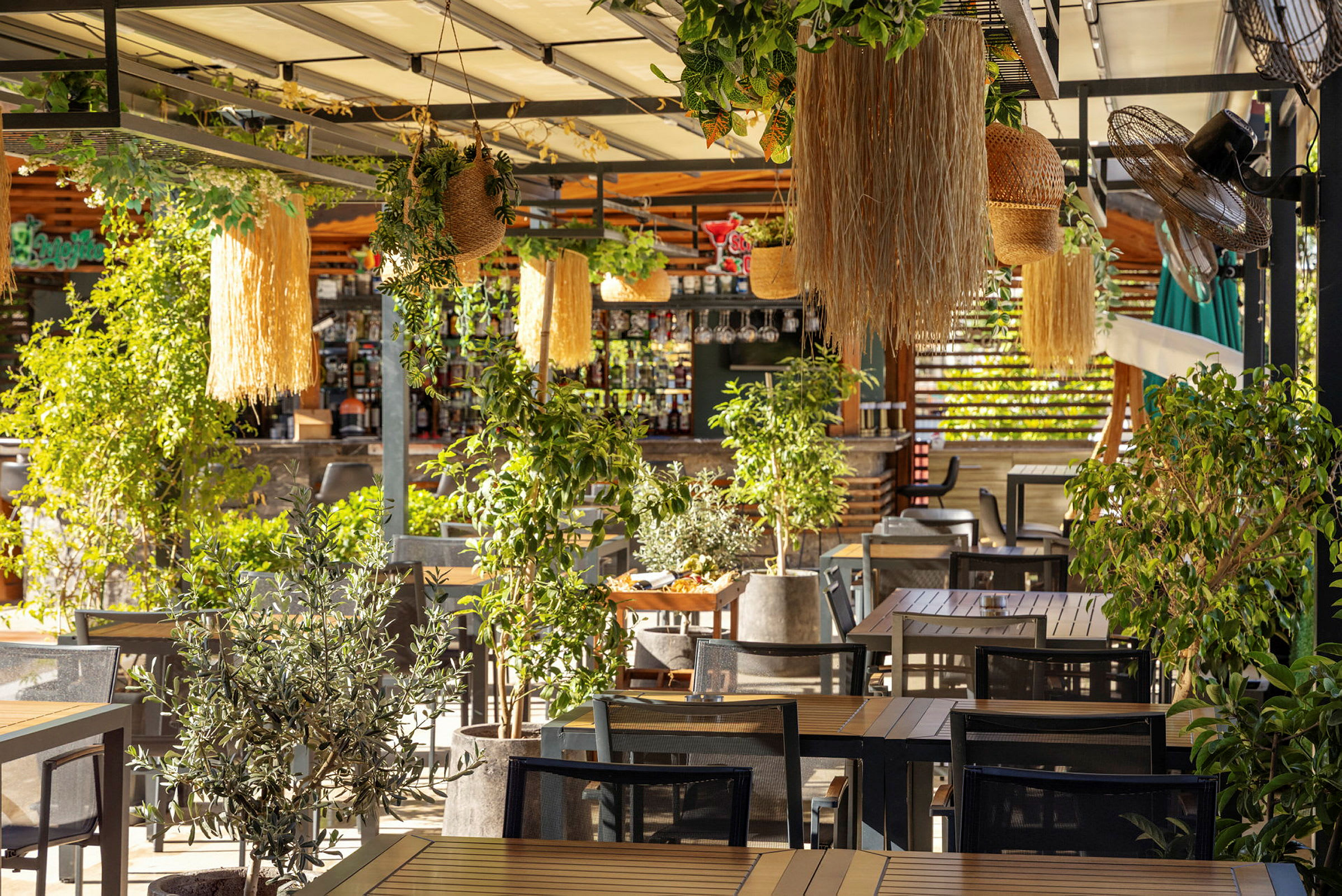 En utomhusrestaurang täckt av växter och dekorationer med träbord och stolar. (AI-genererad text)