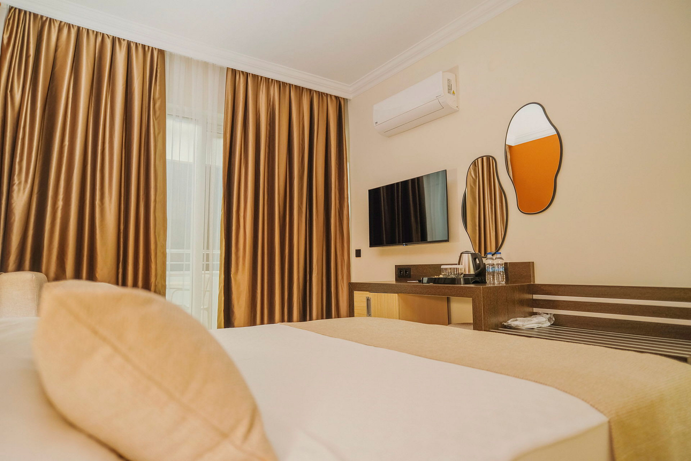 Bilden visar ett hotellrum med en säng i förgrunden, en väggmonterad TV, speglar och en förvaringsmöbel. (AI-genererad text)