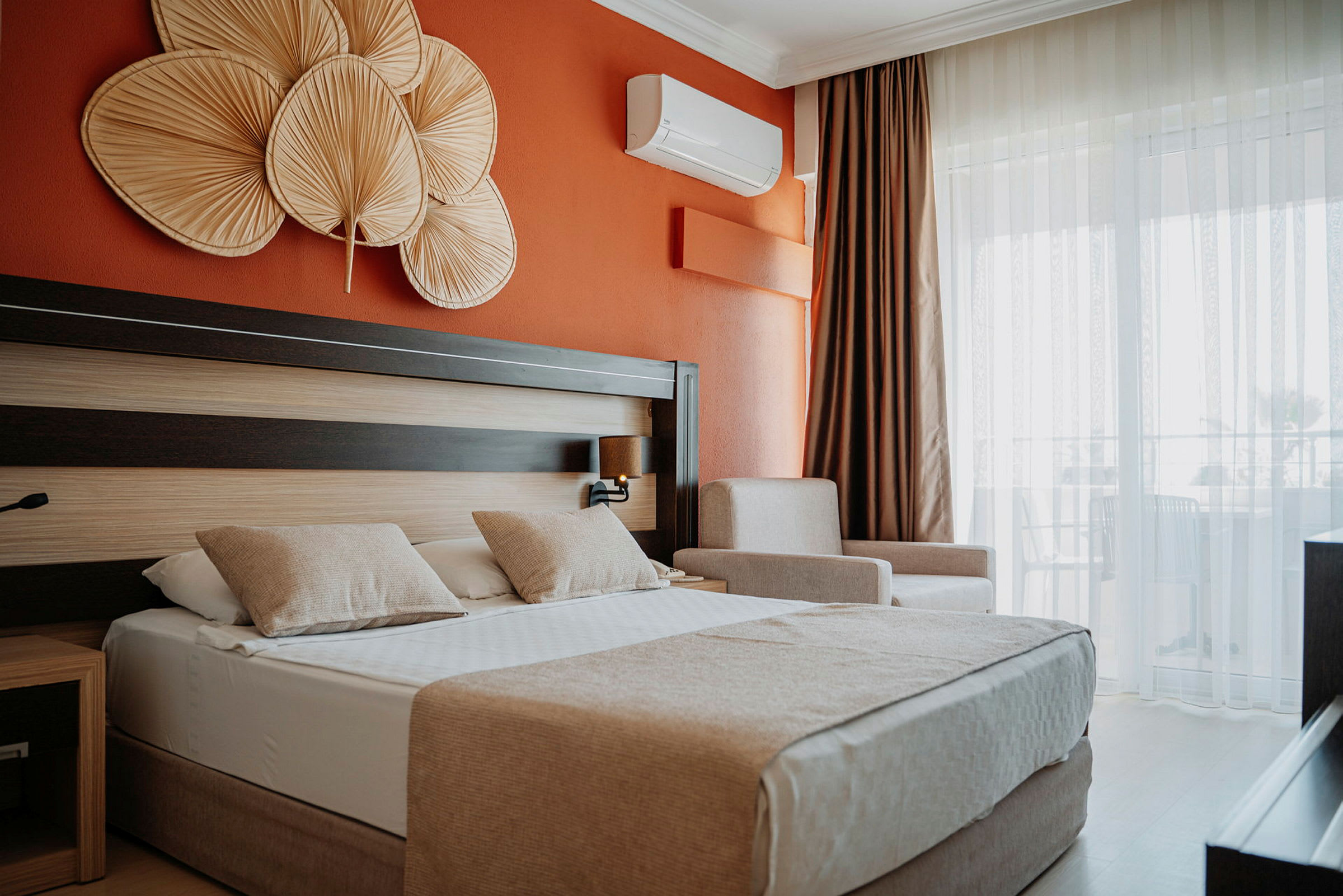 Hotellrum med orange vägg, dubbelsäng med två kuddar och dekorativa föremål ovanför sängen. (AI-genererad text)
