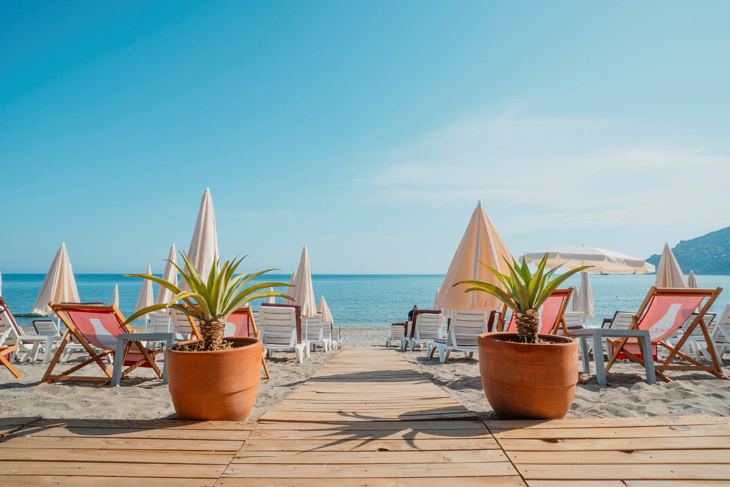 Strand med solstolar, parasoller och två stora krukväxter. (AI-genererad text)