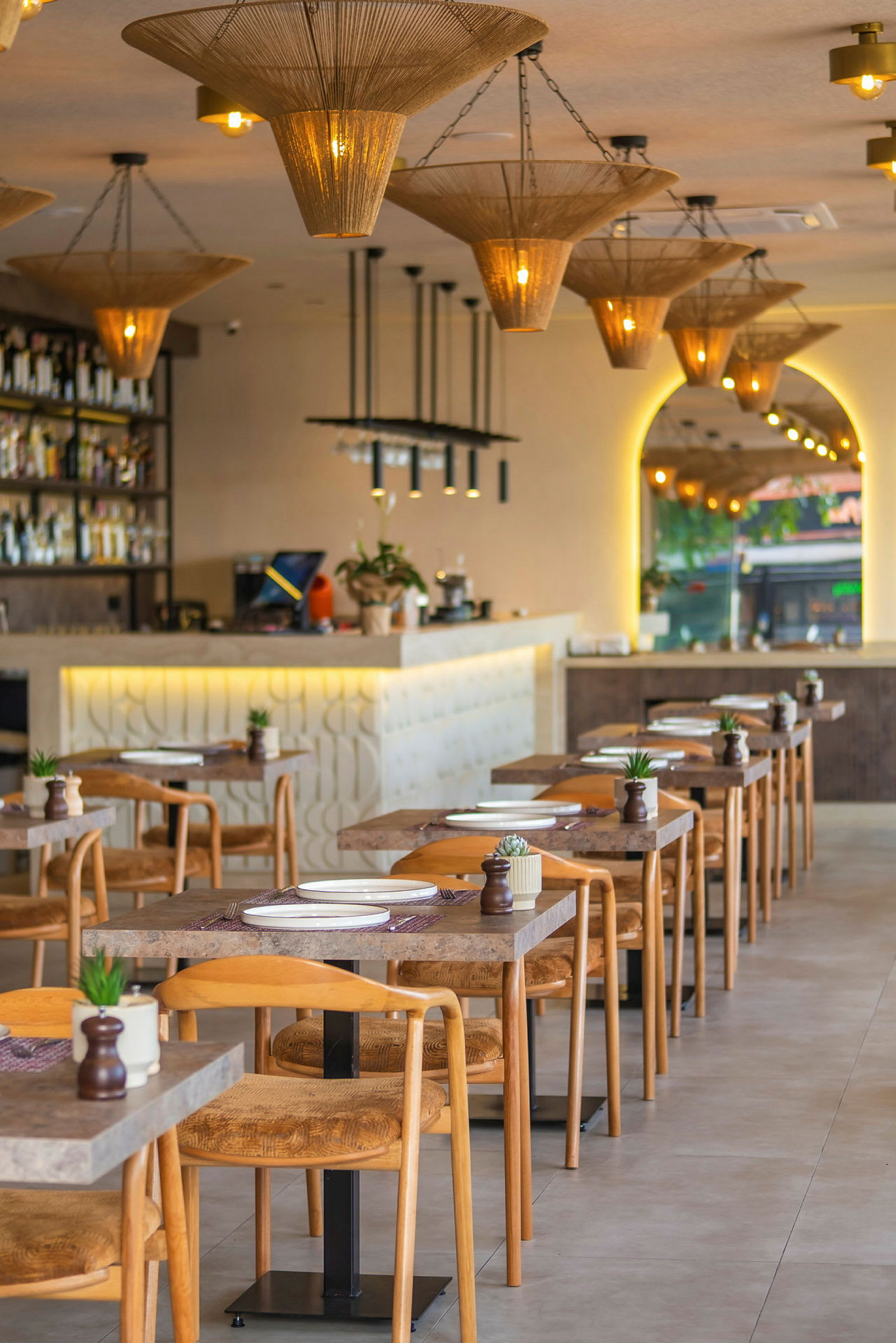Bild av en modern restaurang med uppsatta bord och stolar, samt dekorativa taklampor. (AI-genererad text)