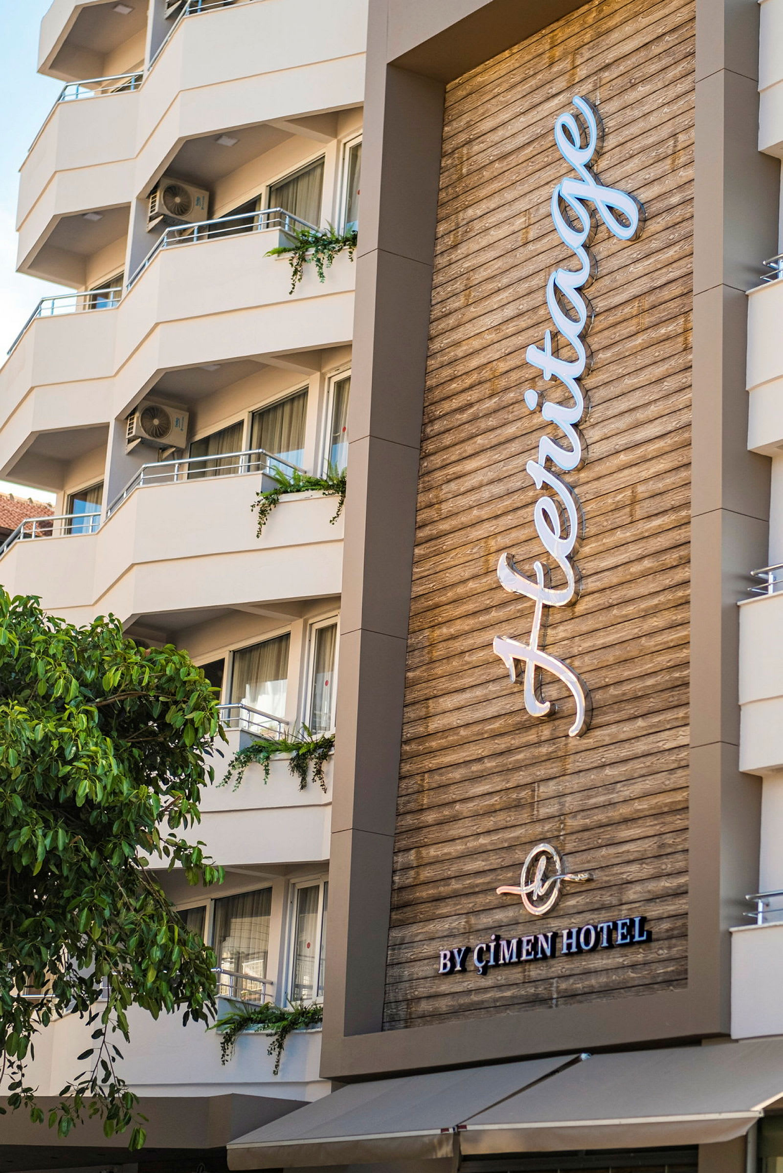 Ett modernt hotell med balkonger och en skylt med texten 'Heritage by Çimen Hotel'. (AI-genererad text)