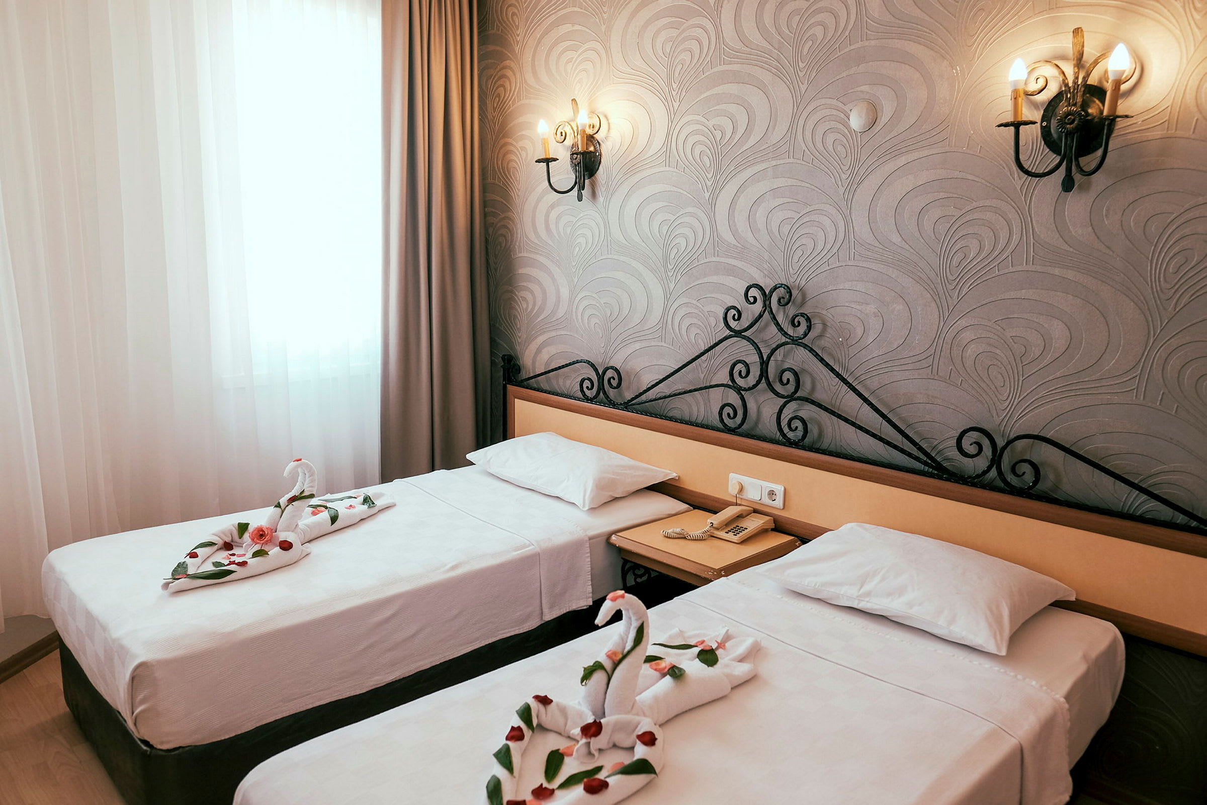 Bild av ett hotellrum med två enkelsängar. Handdukar på sängarna är vikta i form av svanar med dekorativa rosenblad. (AI-genererad text)