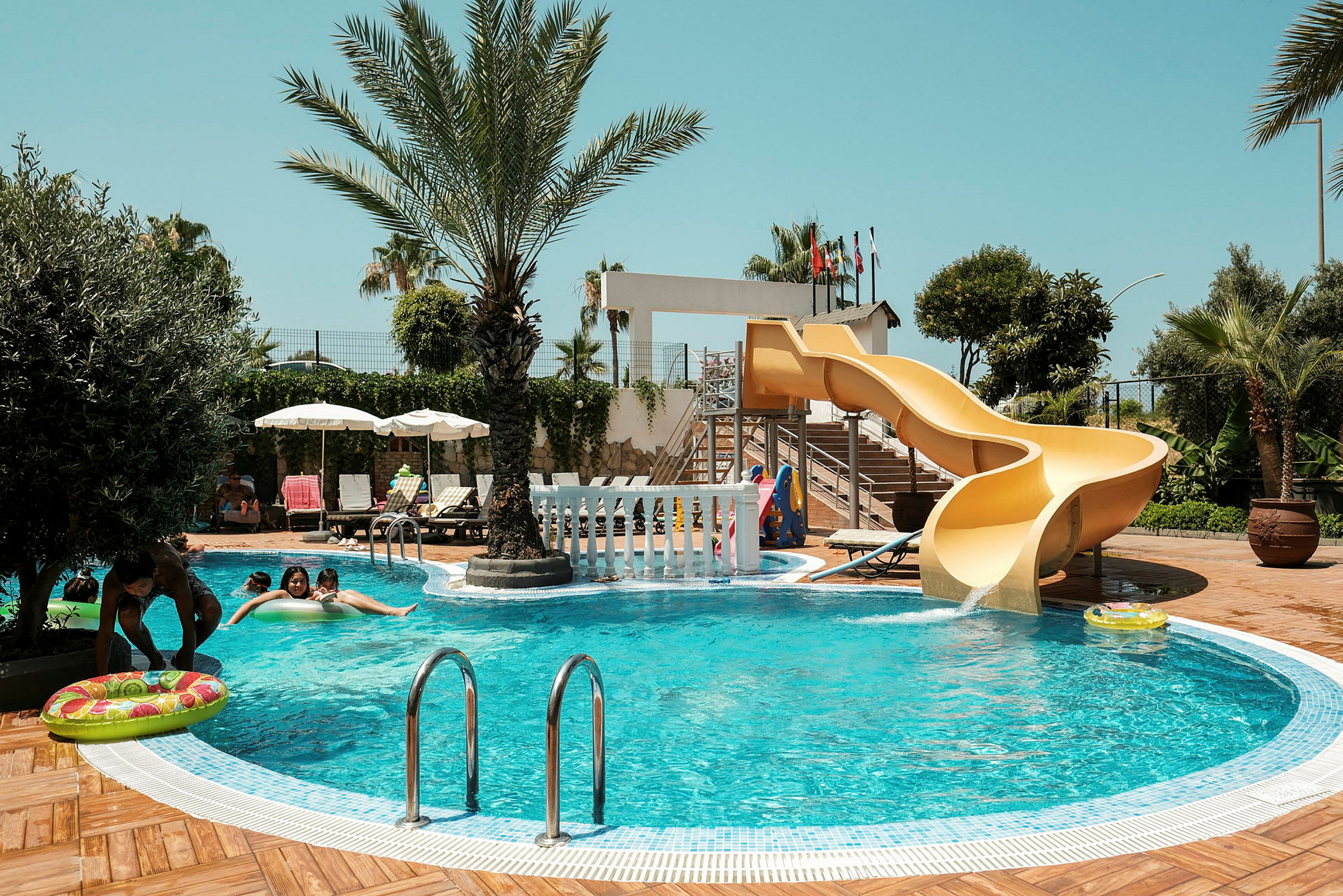 En swimmingpool med en gul vattenrutschkana och omgivna av palmer. (AI-genererad text)