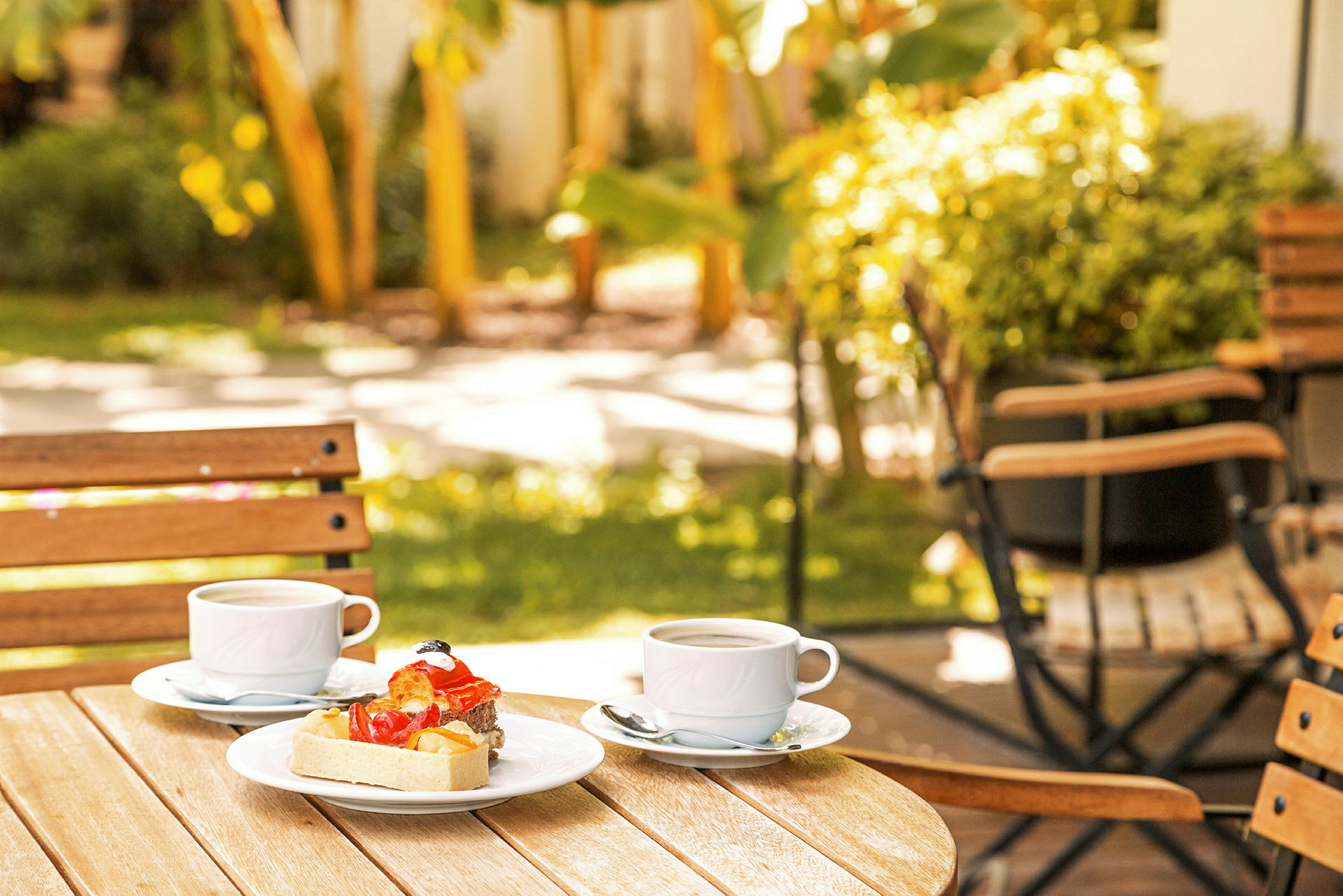 Två kaffekoppar och dessert på ett bord i en trädgård. (AI-genererad text)
