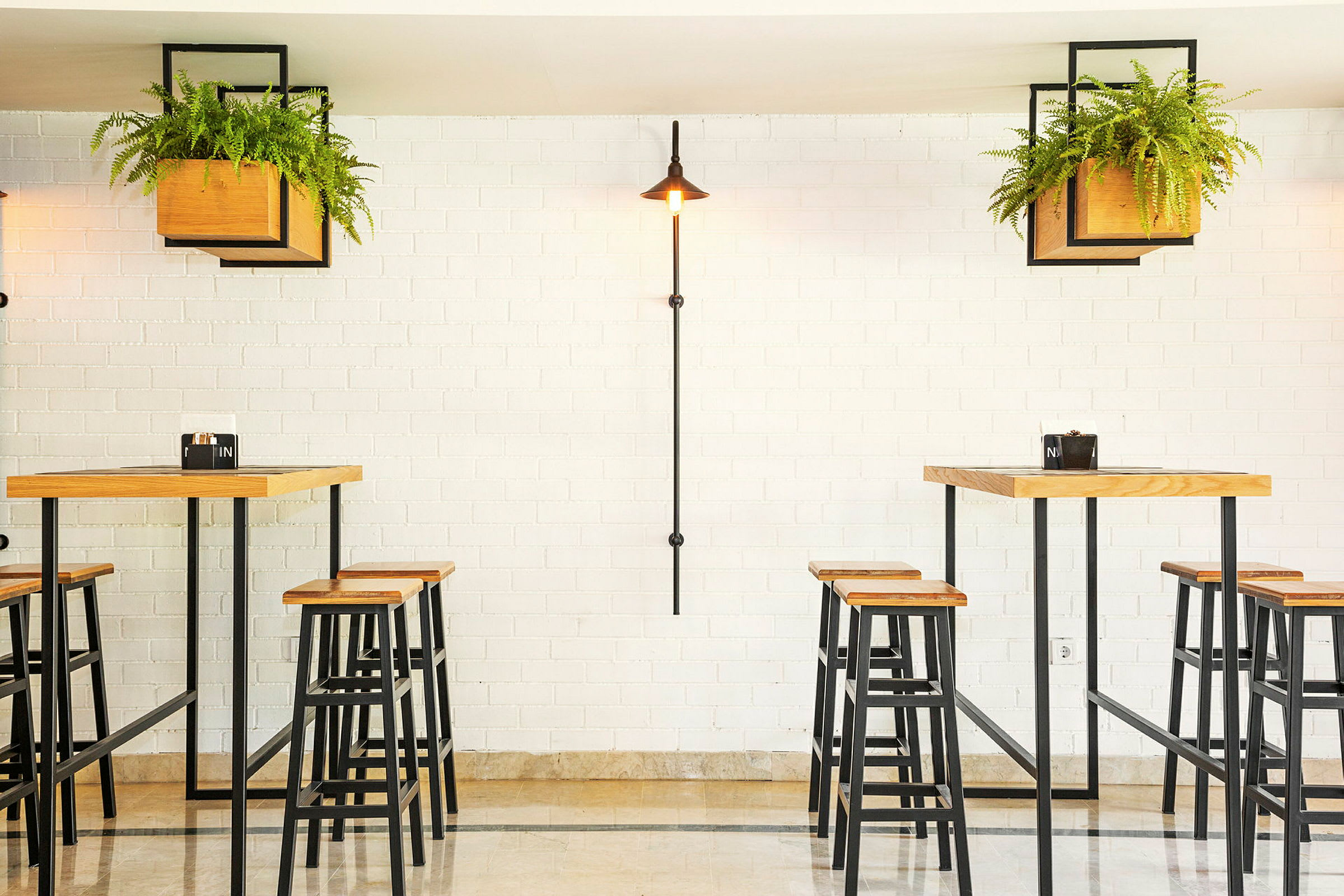 En ljus restaurang med höga bord och pallar, omgiven av gröna växter. (AI-genererad text)
