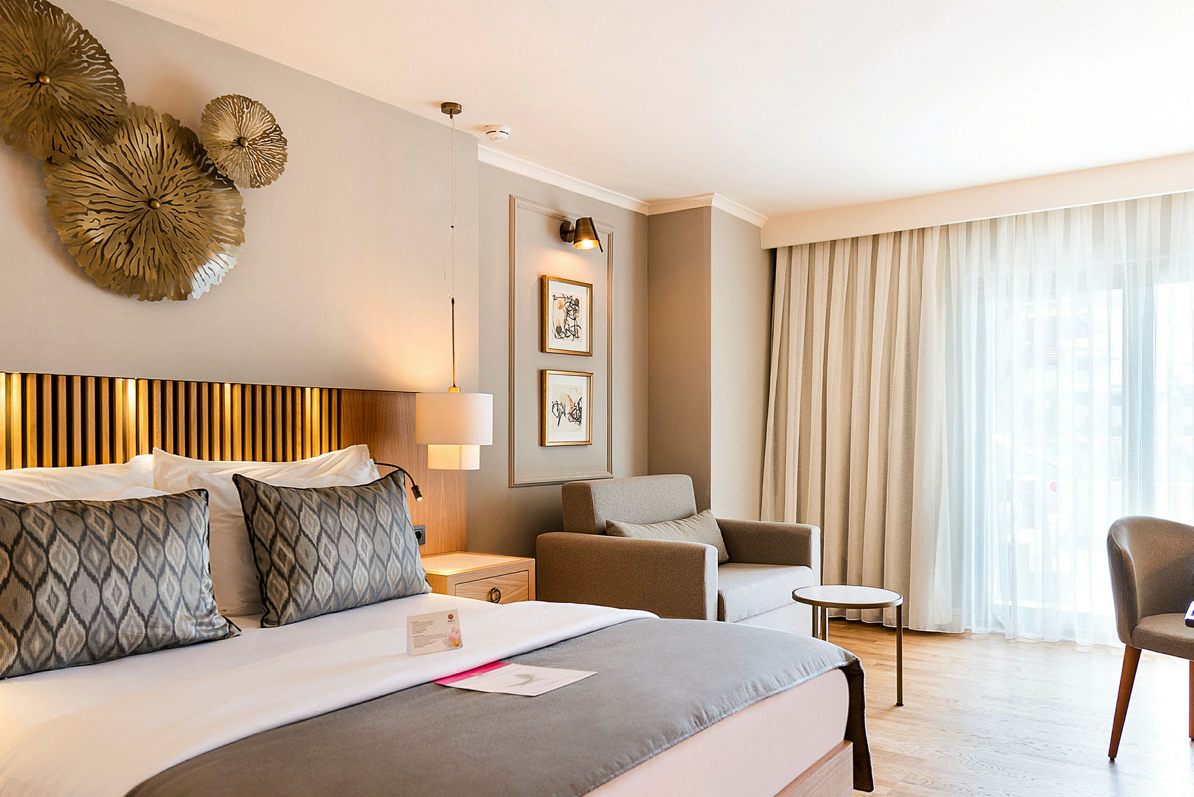 Ett hotellrum med en stor säng, en fåtölj och ett bord vid ett fönster. (AI-genererad text)