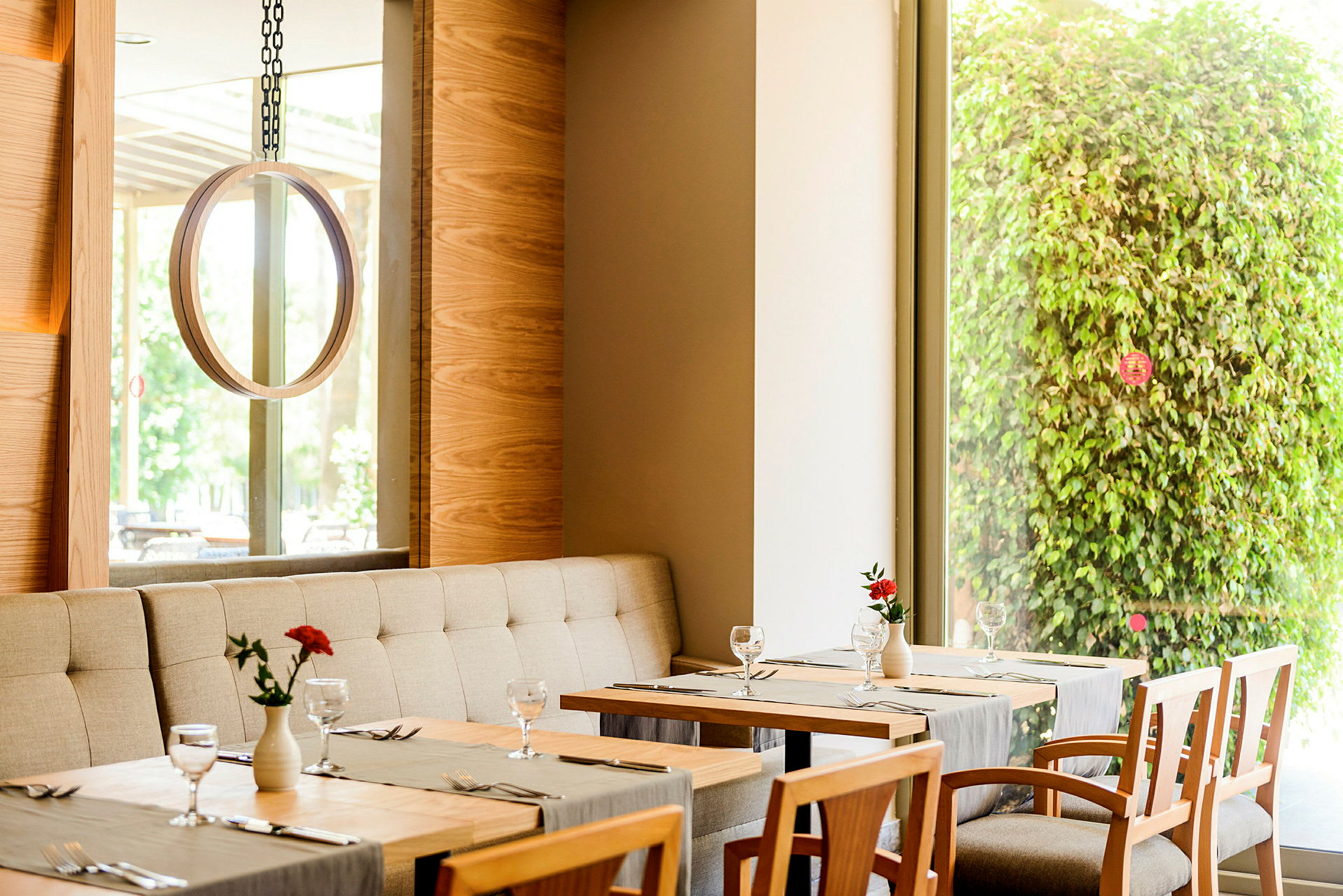 En restauranginteriör med bord, stolar och en grön växtvägg syns genom ett fönster. (AI-genererad text)
