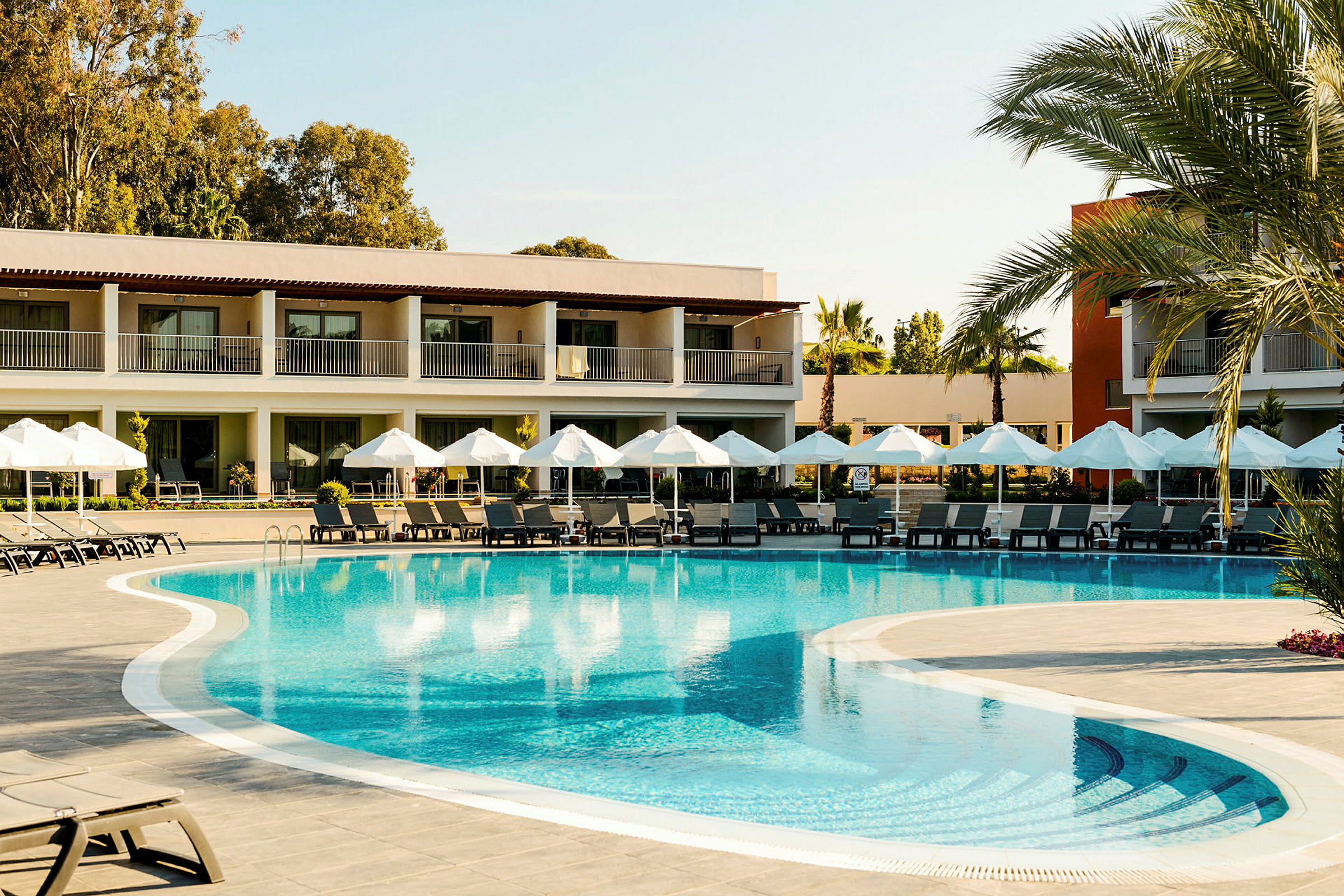 Utomhuspool vid ett hotell omgivet av solstolar och parasoller. (AI-genererad text)