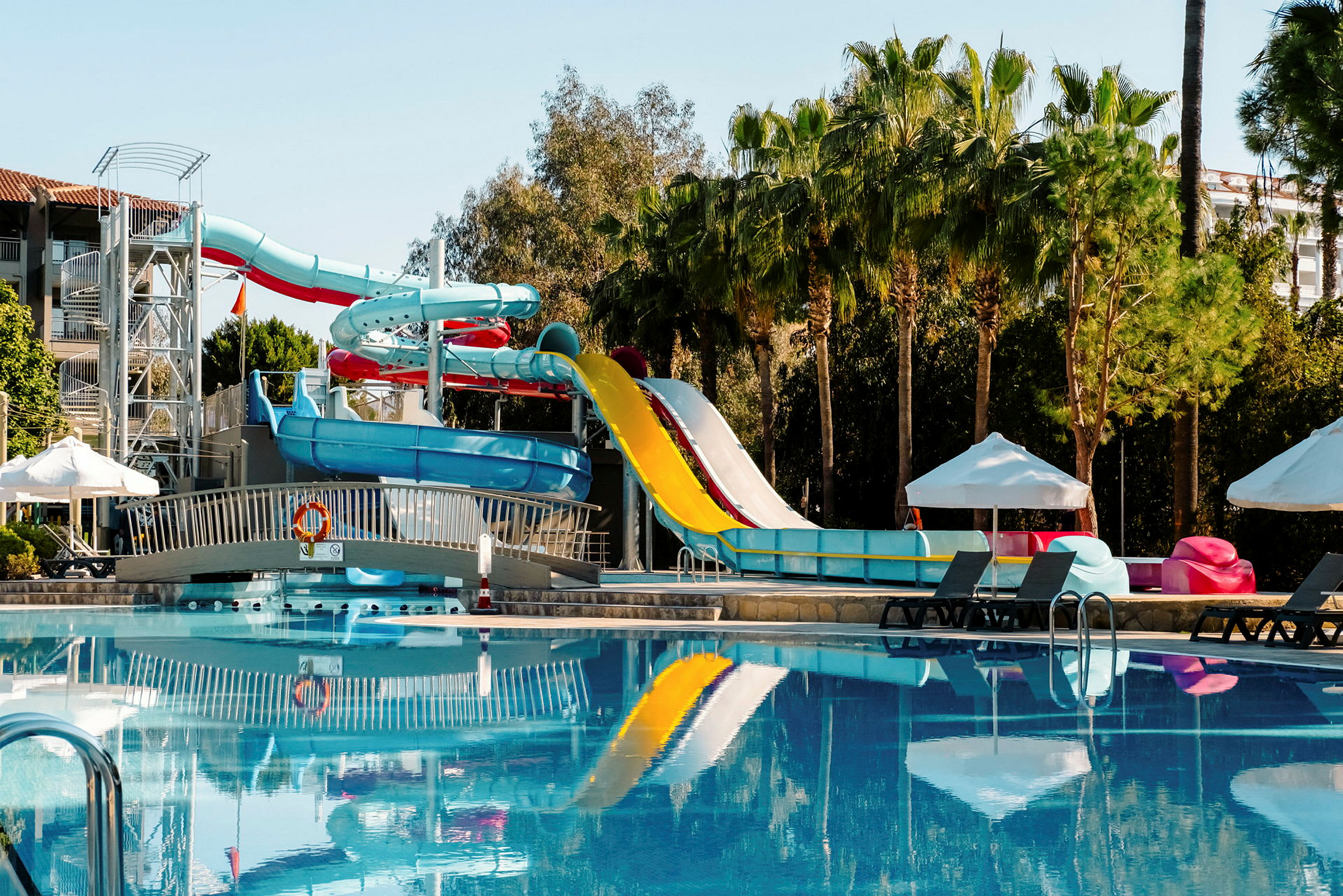 En swimmingpool med vattenrutschbanor och solsängar under parasoll. (AI-genererad text)