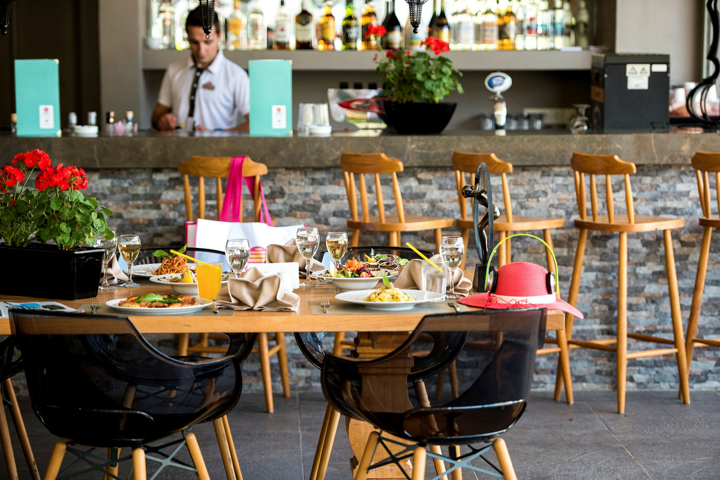 Ett bord fyllt med tallrikar och drycker framför en bar med höga stolar. (AI-genererad text)