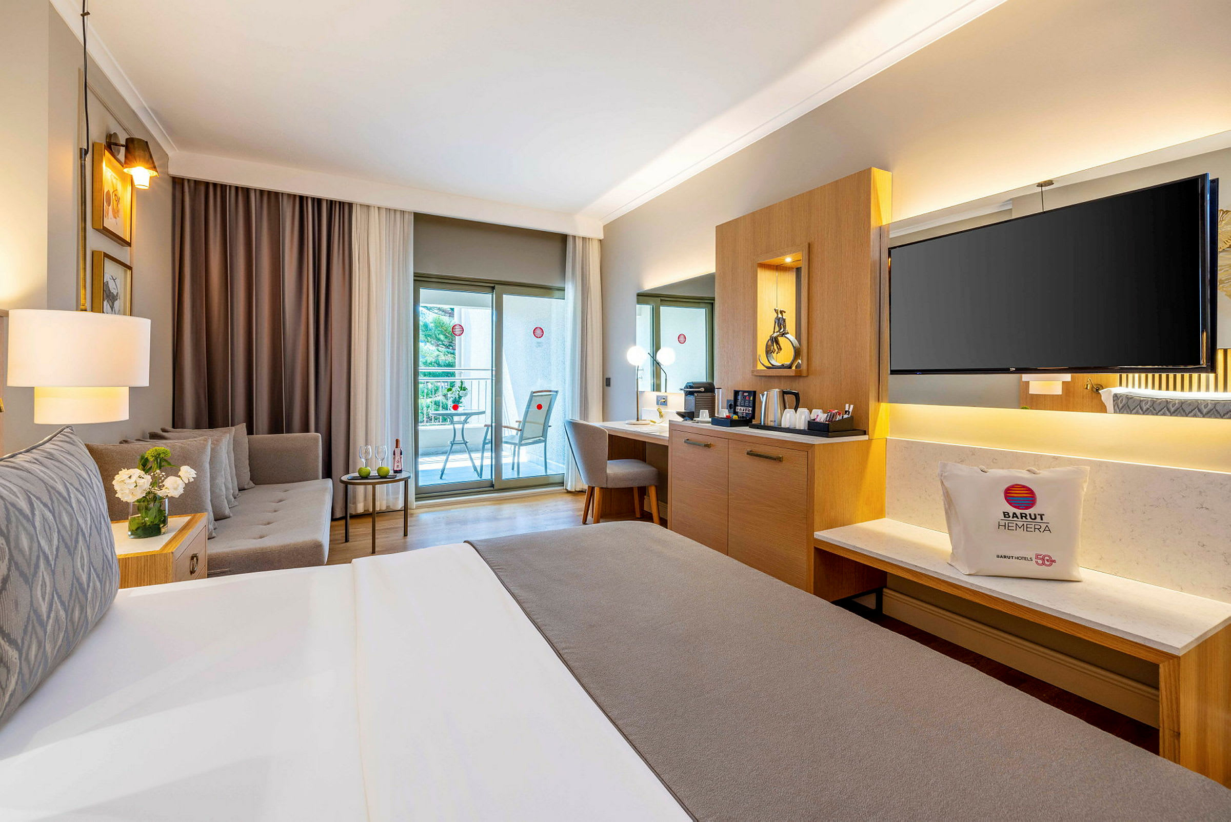 Ett välmöblerat hotellrum med en dubbelsäng, sittgrupp, skrivbord och en balkong. (AI-genererad text)