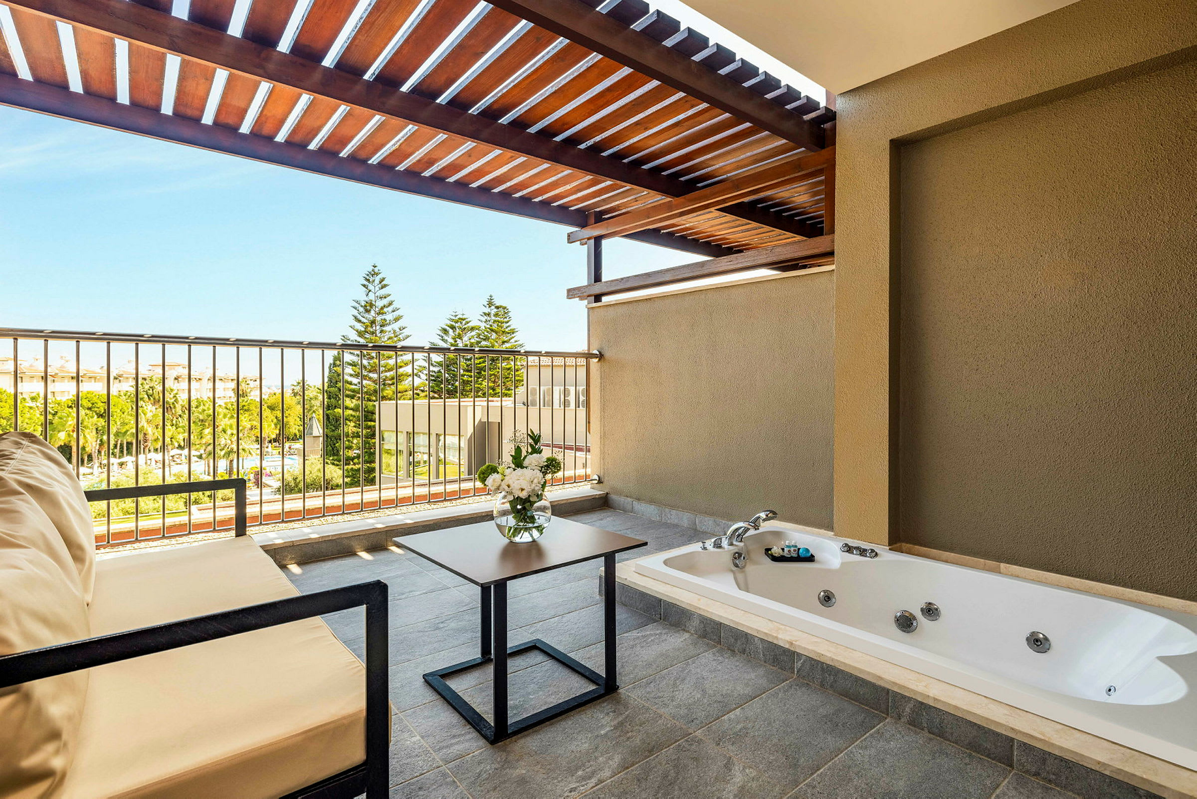 En terrass med jacuzzi, sittmöbler, blombukett och utsikt över grönska. (AI-genererad text)